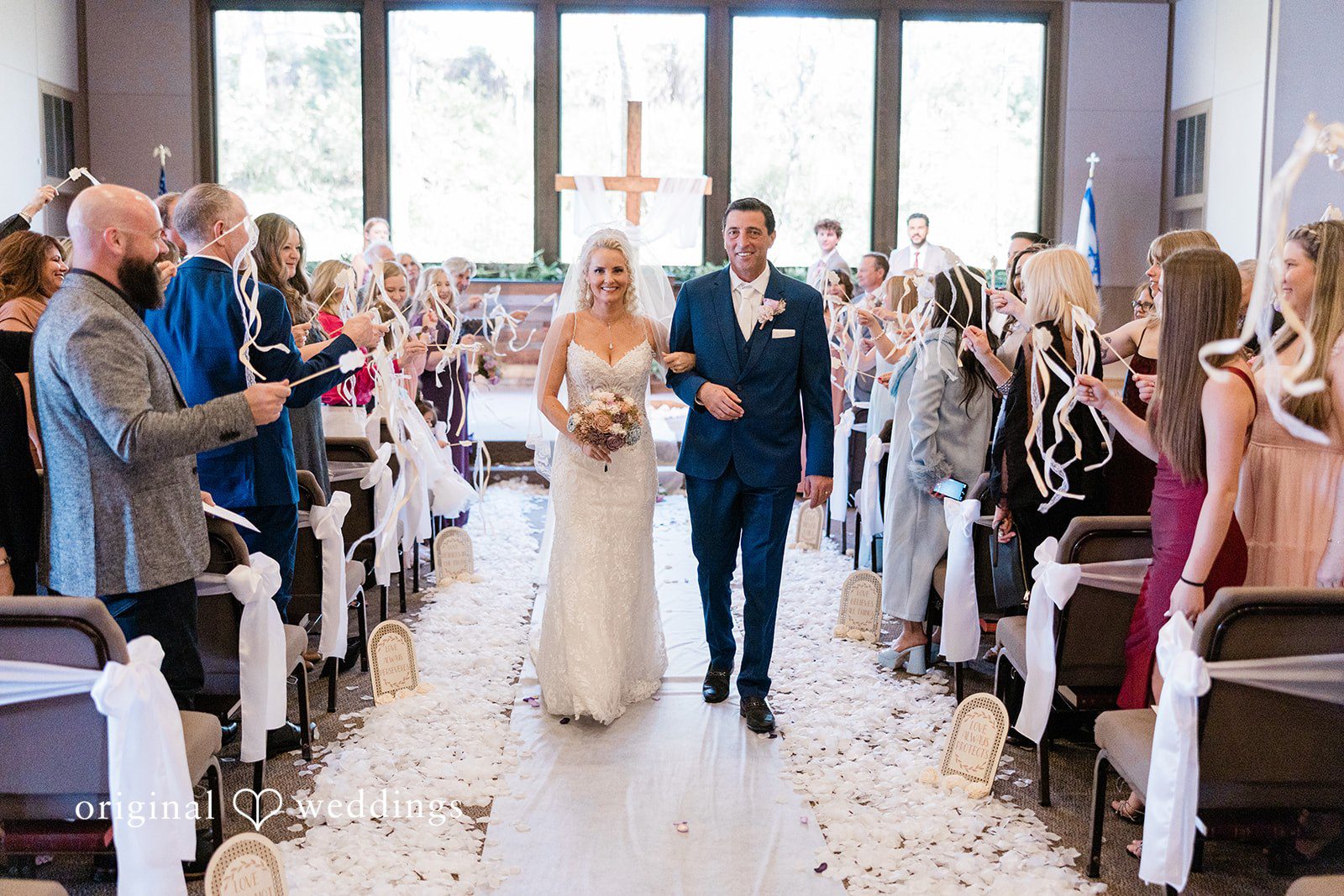 Bride and groom walking down the aisle together as guests smile and look on.