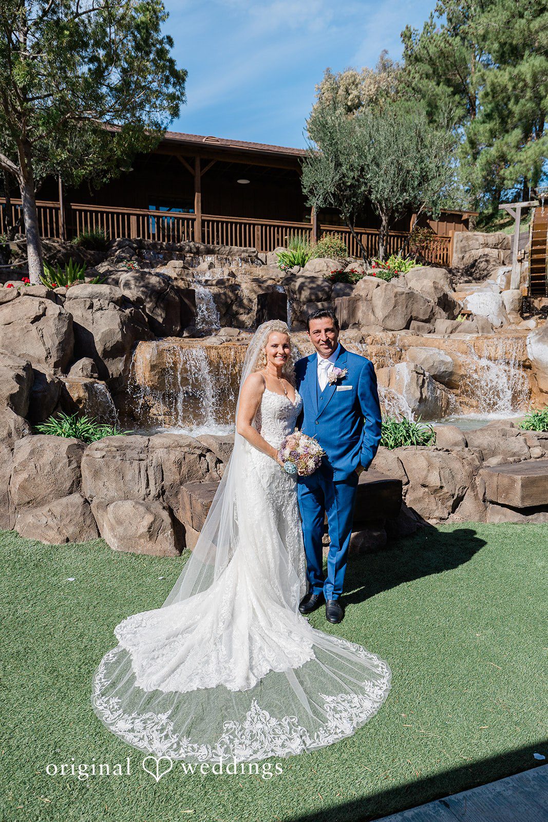 Couple standing together outside in front of a stone waterfall feature.