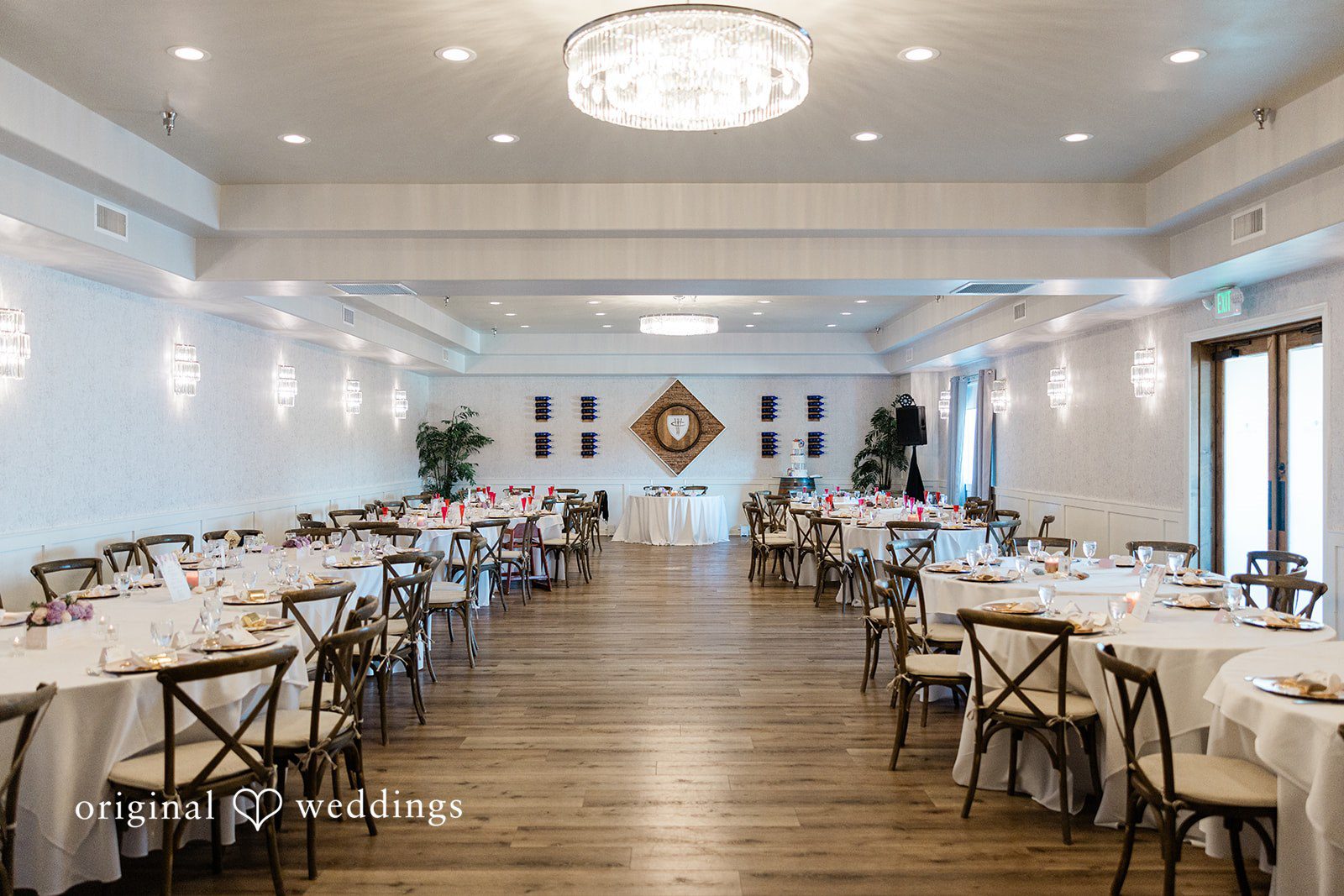 Reception hall with long banquet tables, wooden chairs, and overhead lighting.
