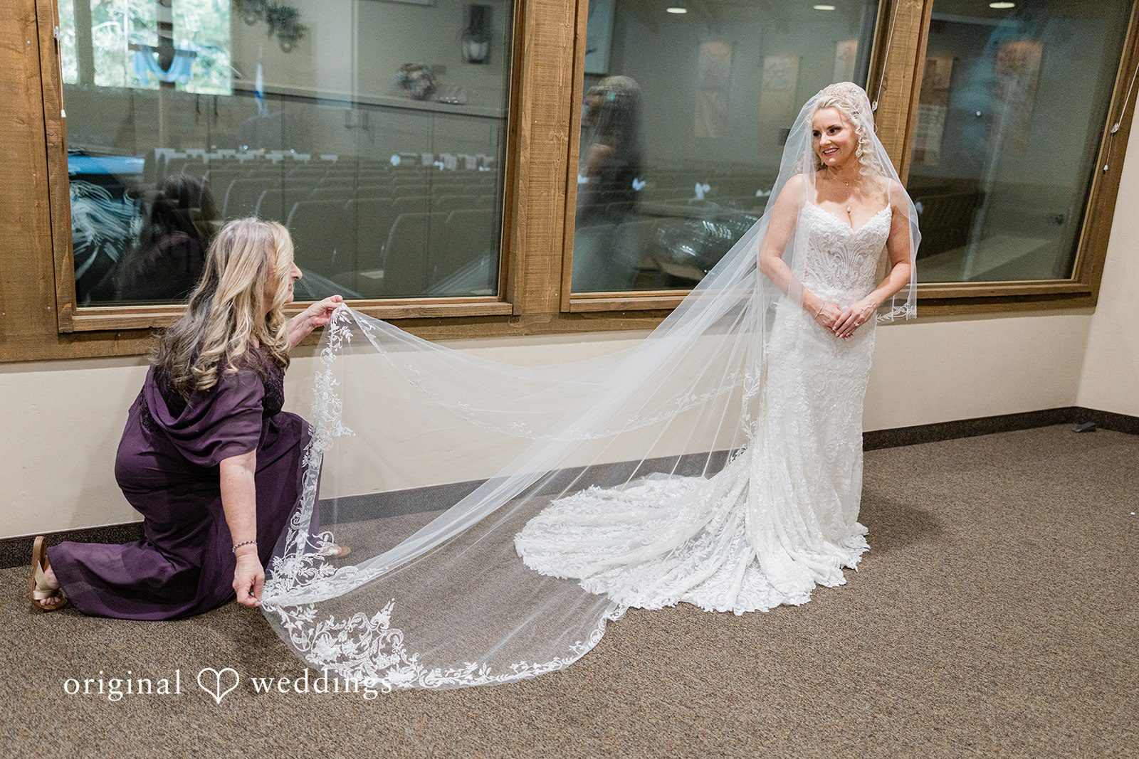 A Girl adjusting the long lace veil of a bride wearing a white wedding gown.