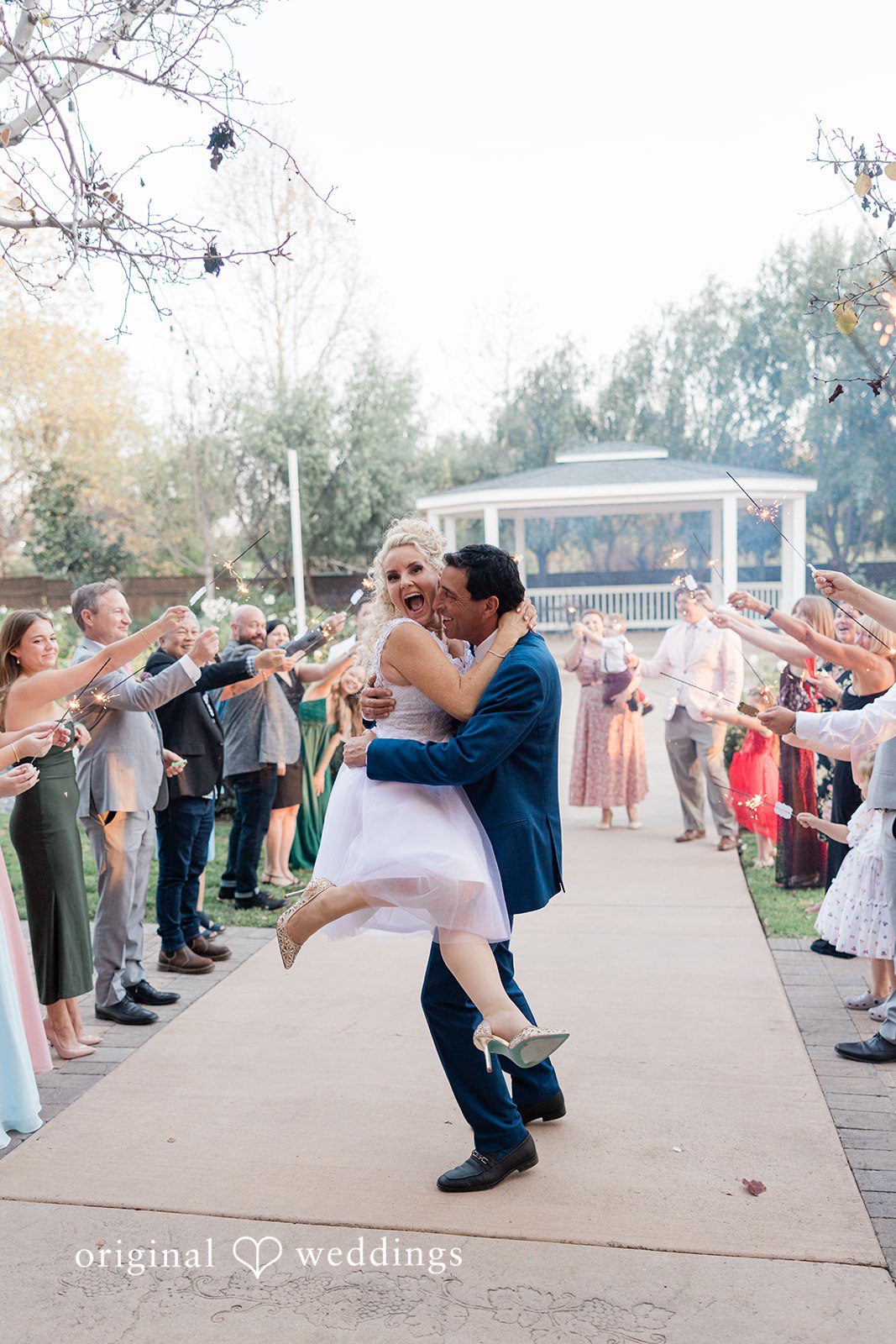 Groom lifting and spinning the bride during a grand exit celebration surrounded by guests.