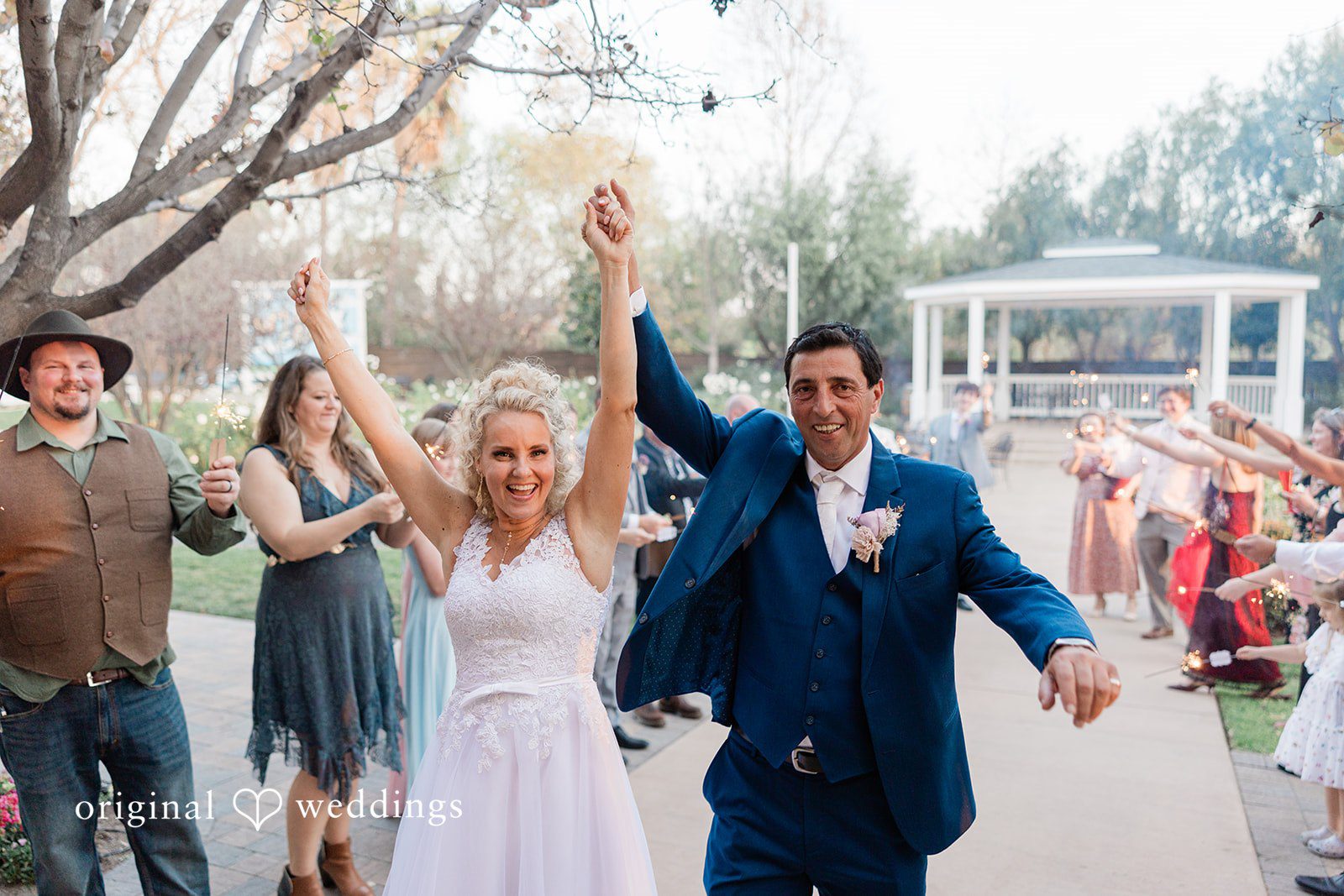 Couple  cheering with their arms raised as they walk through a cheering crowd of guests.