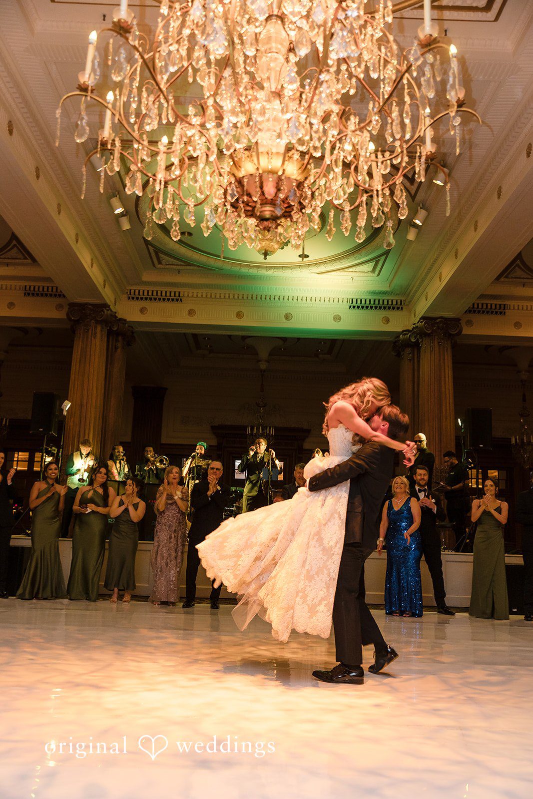 The couple shares a romantic kiss beneath the warm chandelier glow