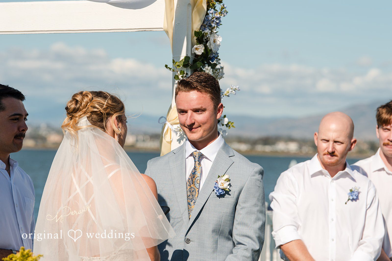 Elegant groom under floral ceremony arch at waterfront venue