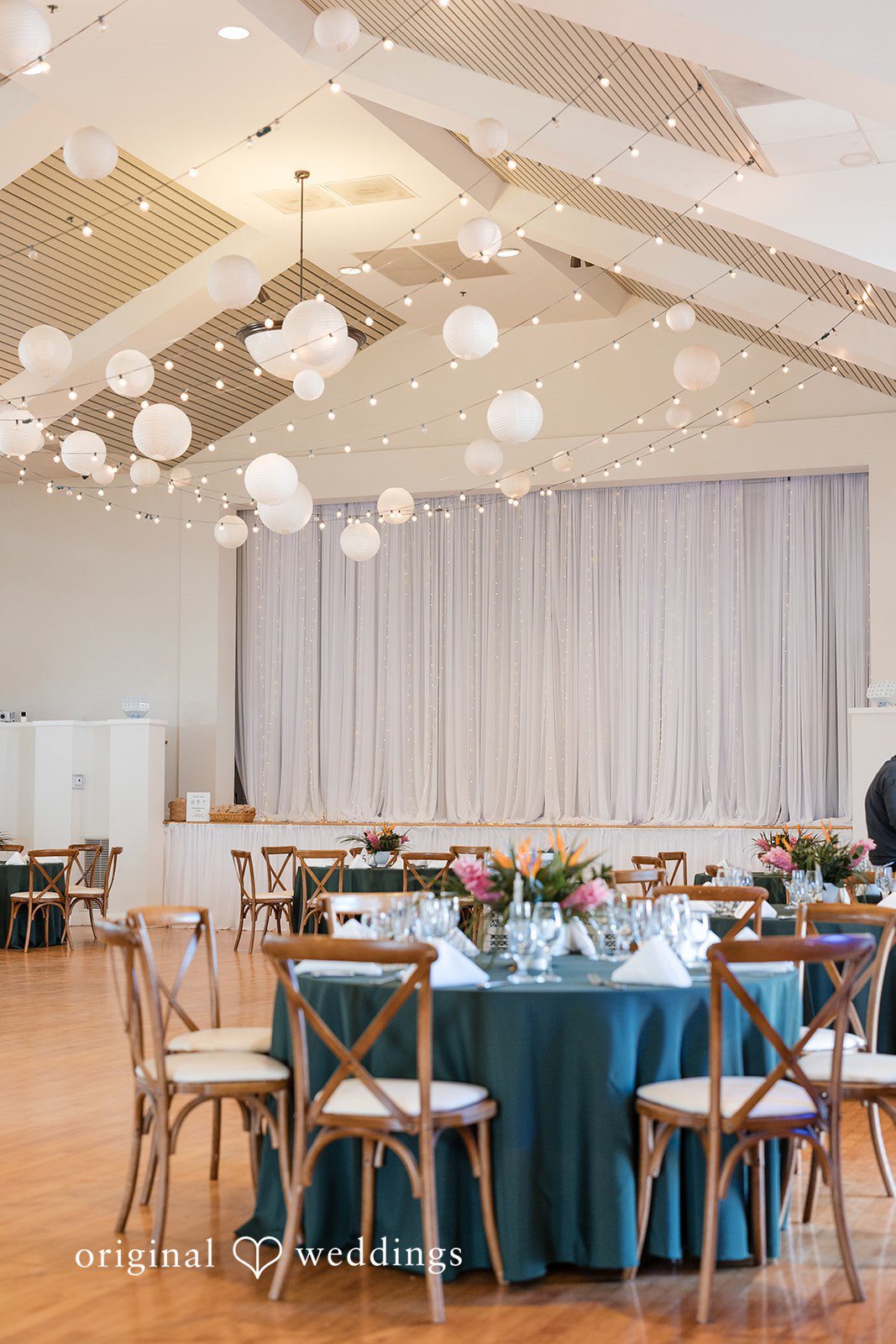 Wedding reception layout featuring round tables with teal tablecloths and wooden chairs.