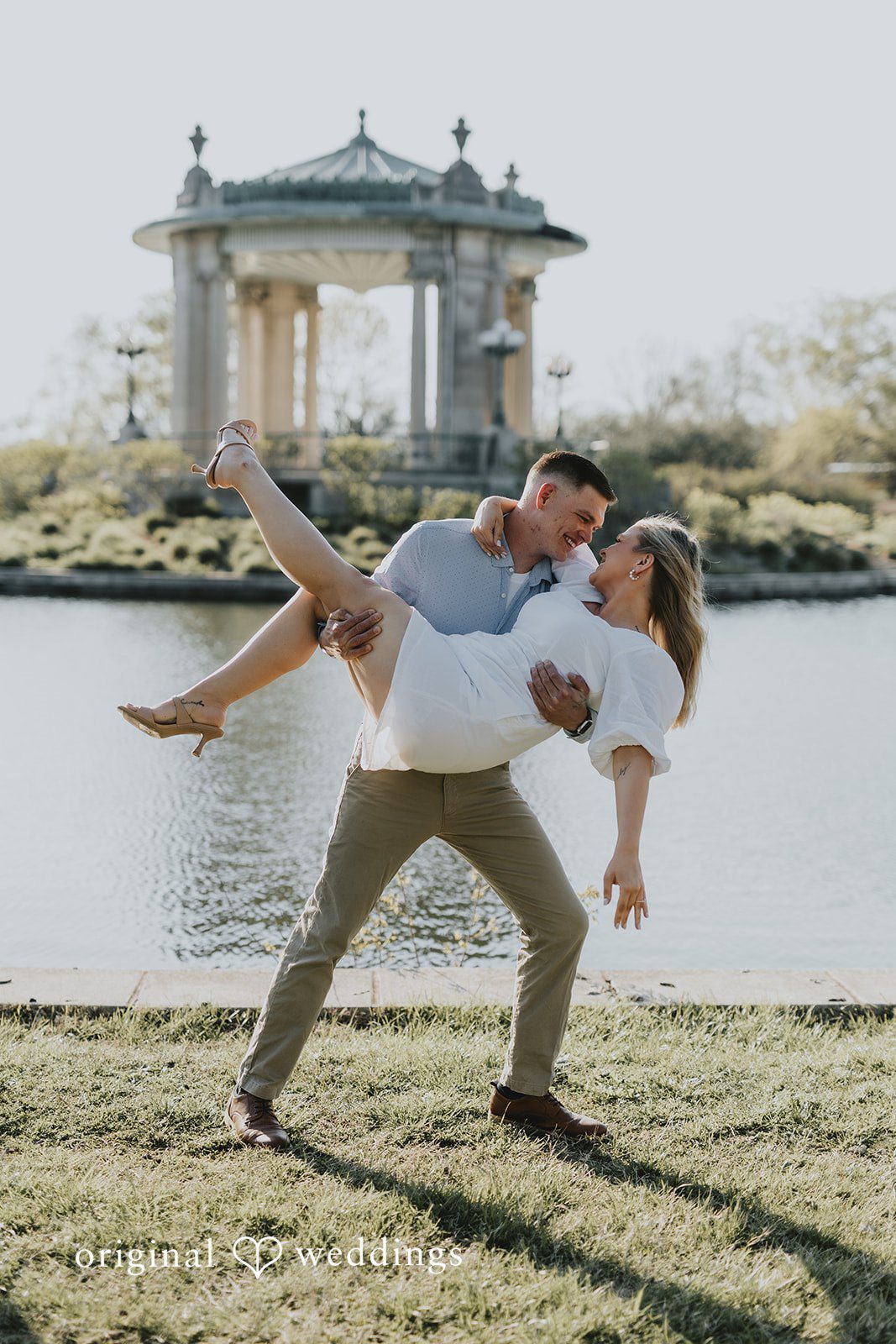 The groom carries the bride by the waterfront