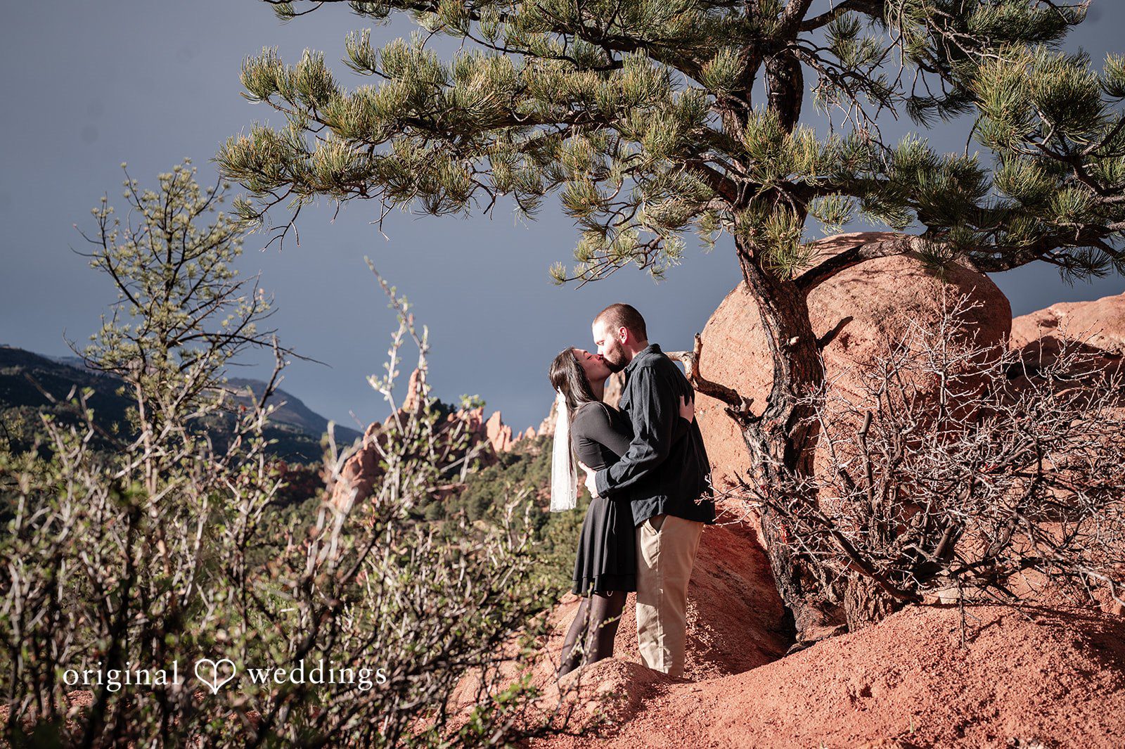 The couple shares a kiss by the red rocks formations at the venue