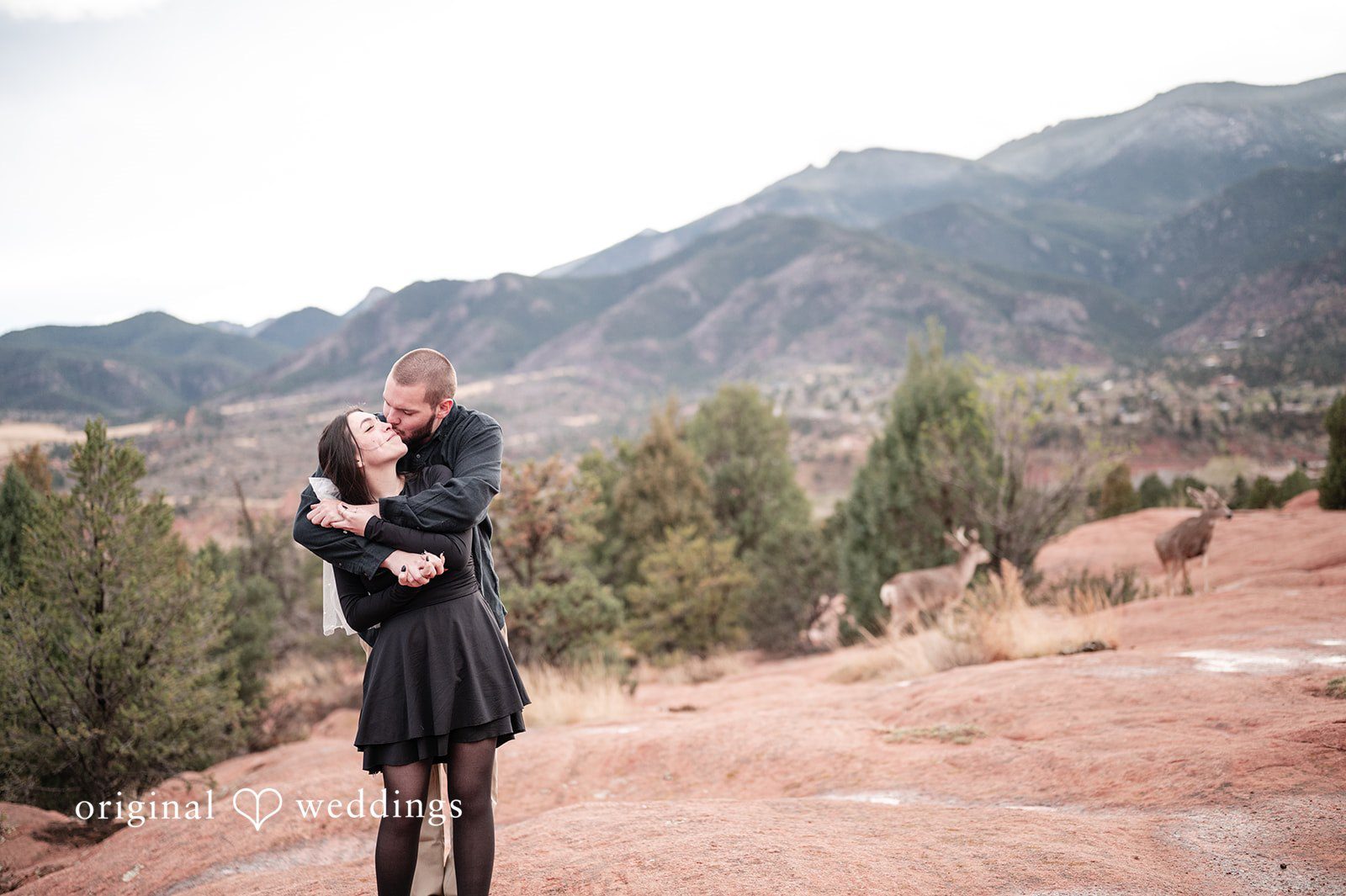 The couple shares a romantic kiss amidst the mountains and red rocks