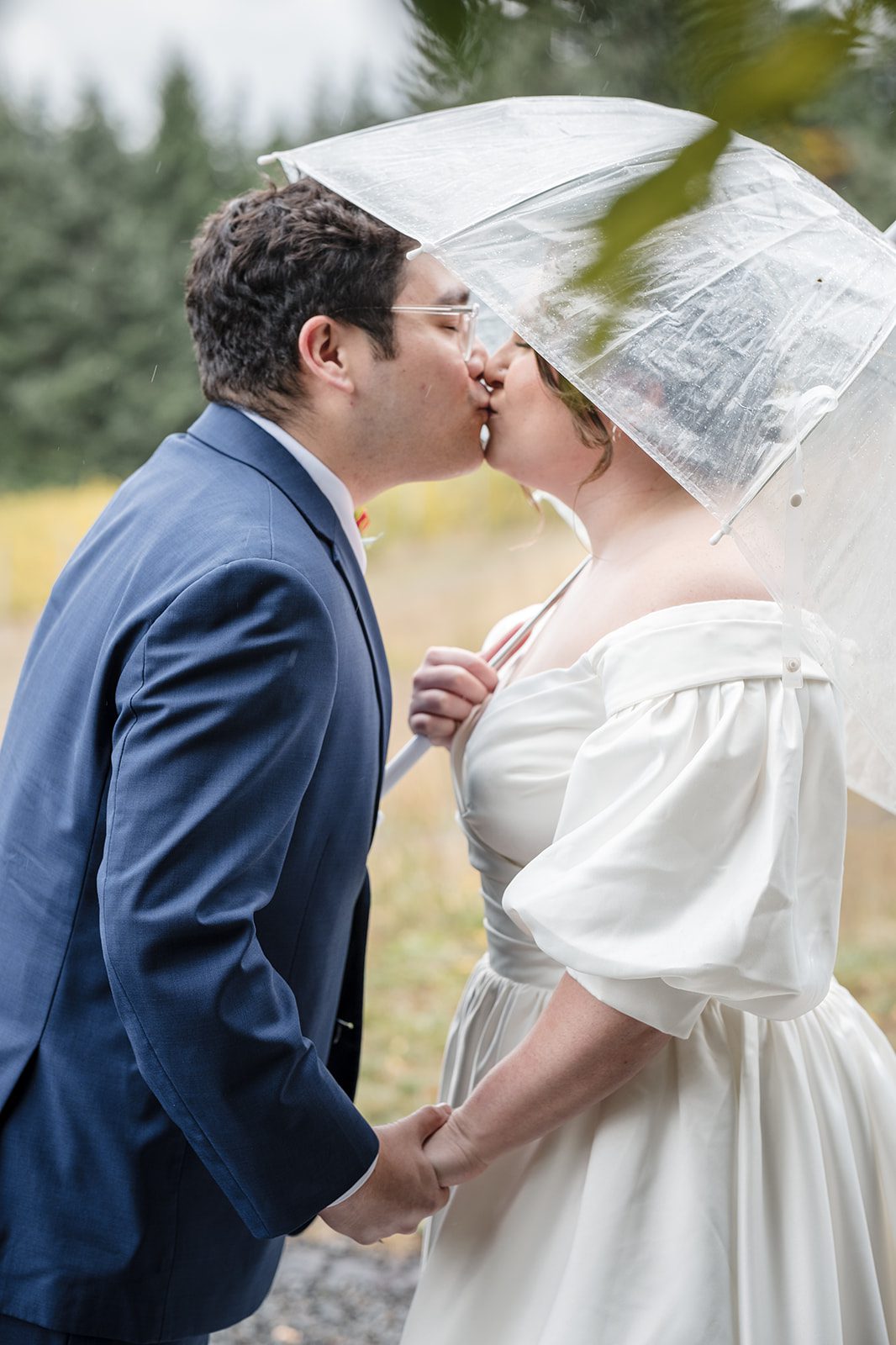 Tiare + Jeremy Bride and groom kissing beneath a clear umbrella during a rainy vineyard wedding portrait session