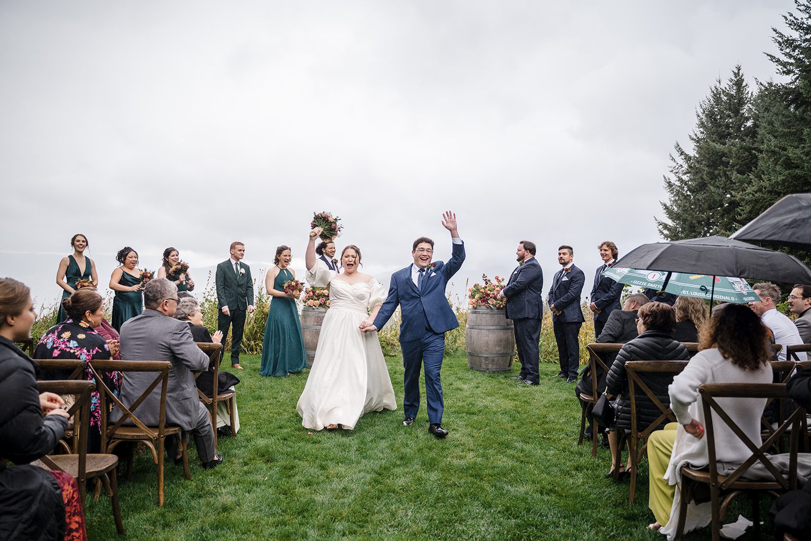Tiare + Jeremy Bride and groom walking down the aisle during an outdoor vineyard wedding ceremony surrounded by guests on a cloudy day