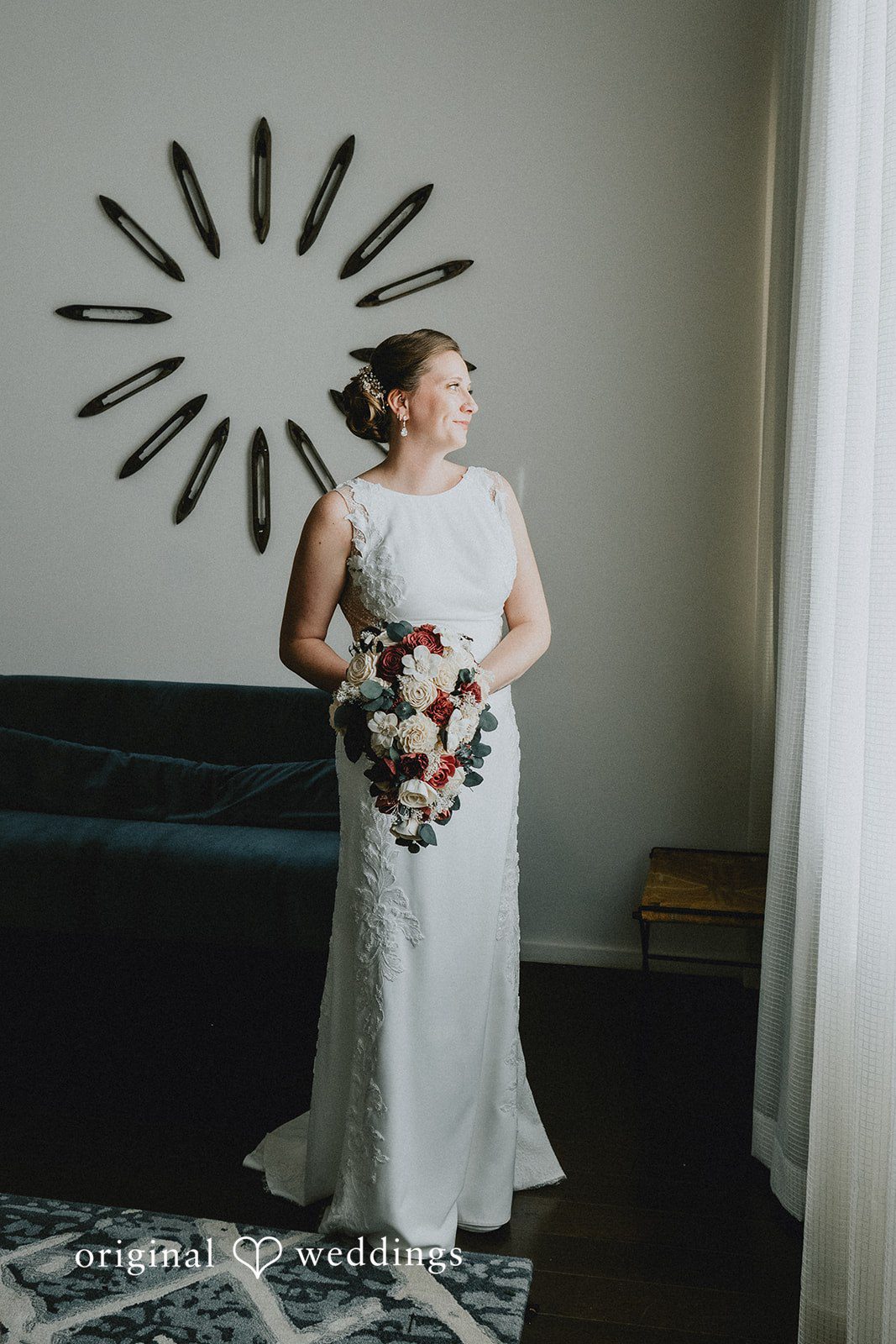 A bride in a white gown holding a bouquet stands in front of a wall with a unique sunburst design.