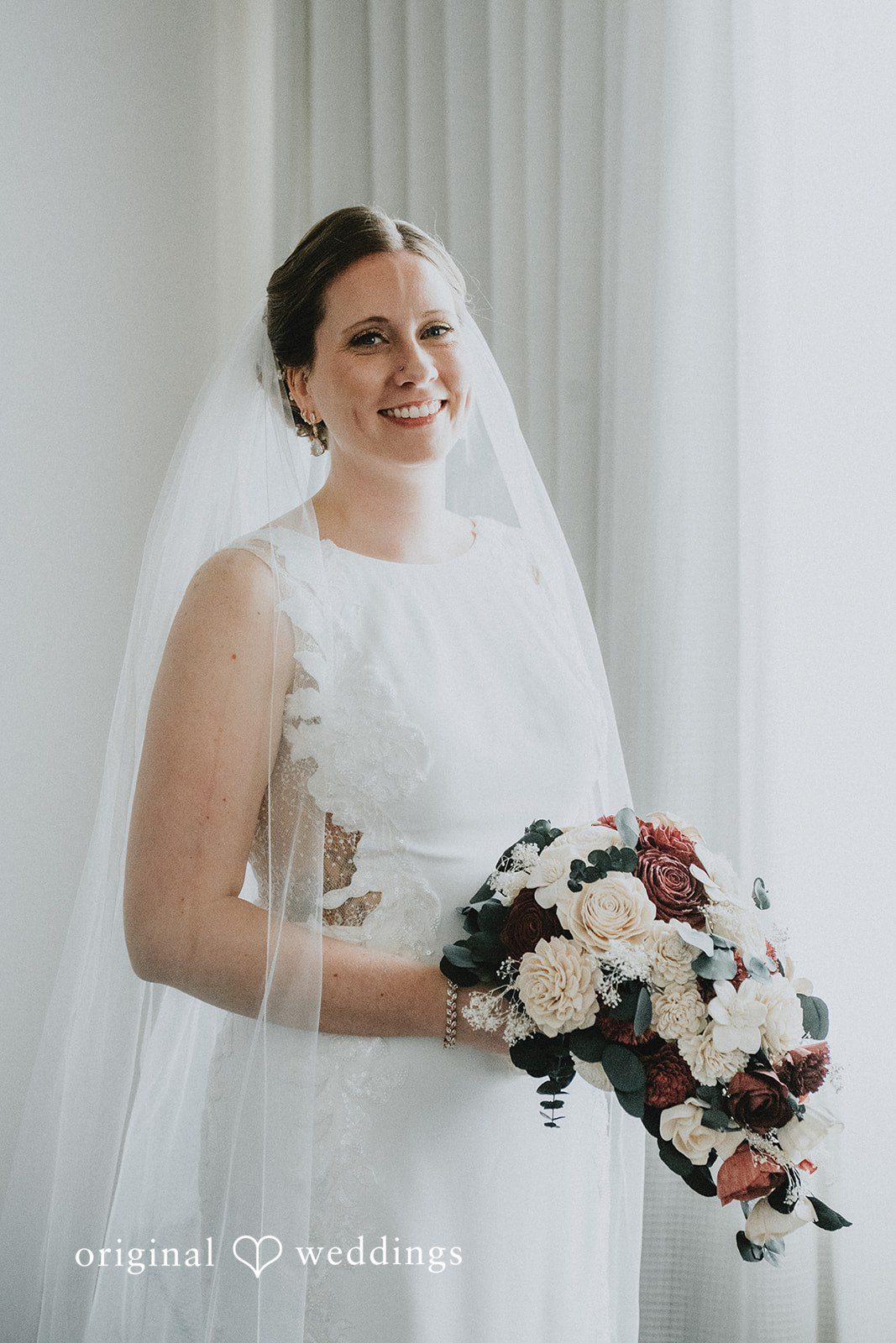 A close-up portrait of the bride smiling and holding her floral bouquet.