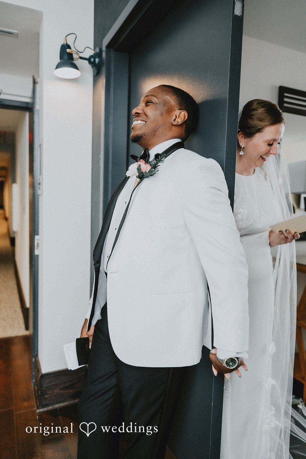 The groom in a white tuxedo jacket laughing with the bride standing just behind him.