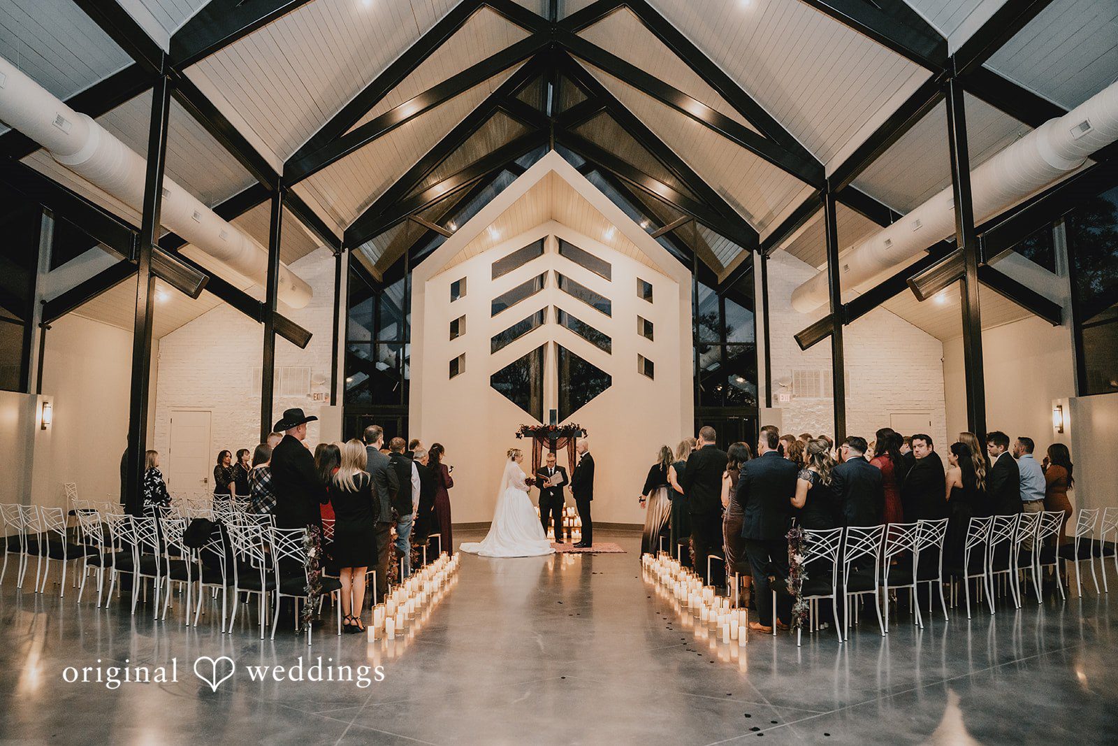 Wedding ceremony in progress with guests seated in rows facing a large geometric altar structure.