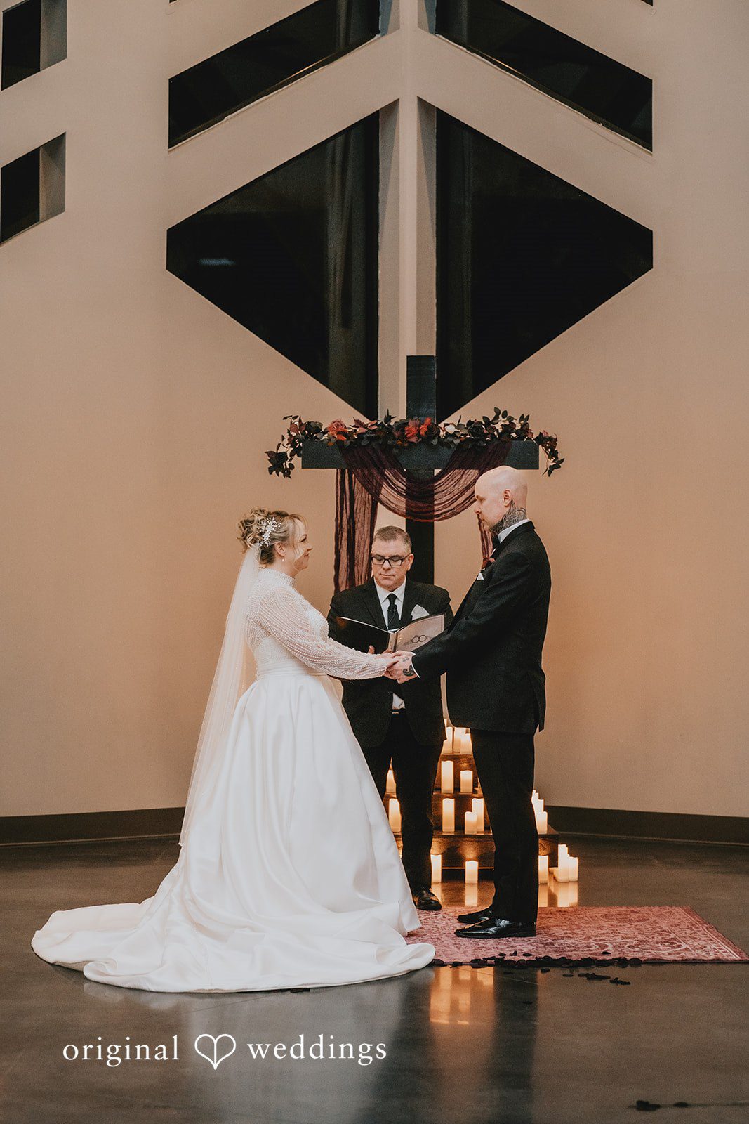 Couple holding hands during their wedding ceremony in front of a dark wooden cross altar.
