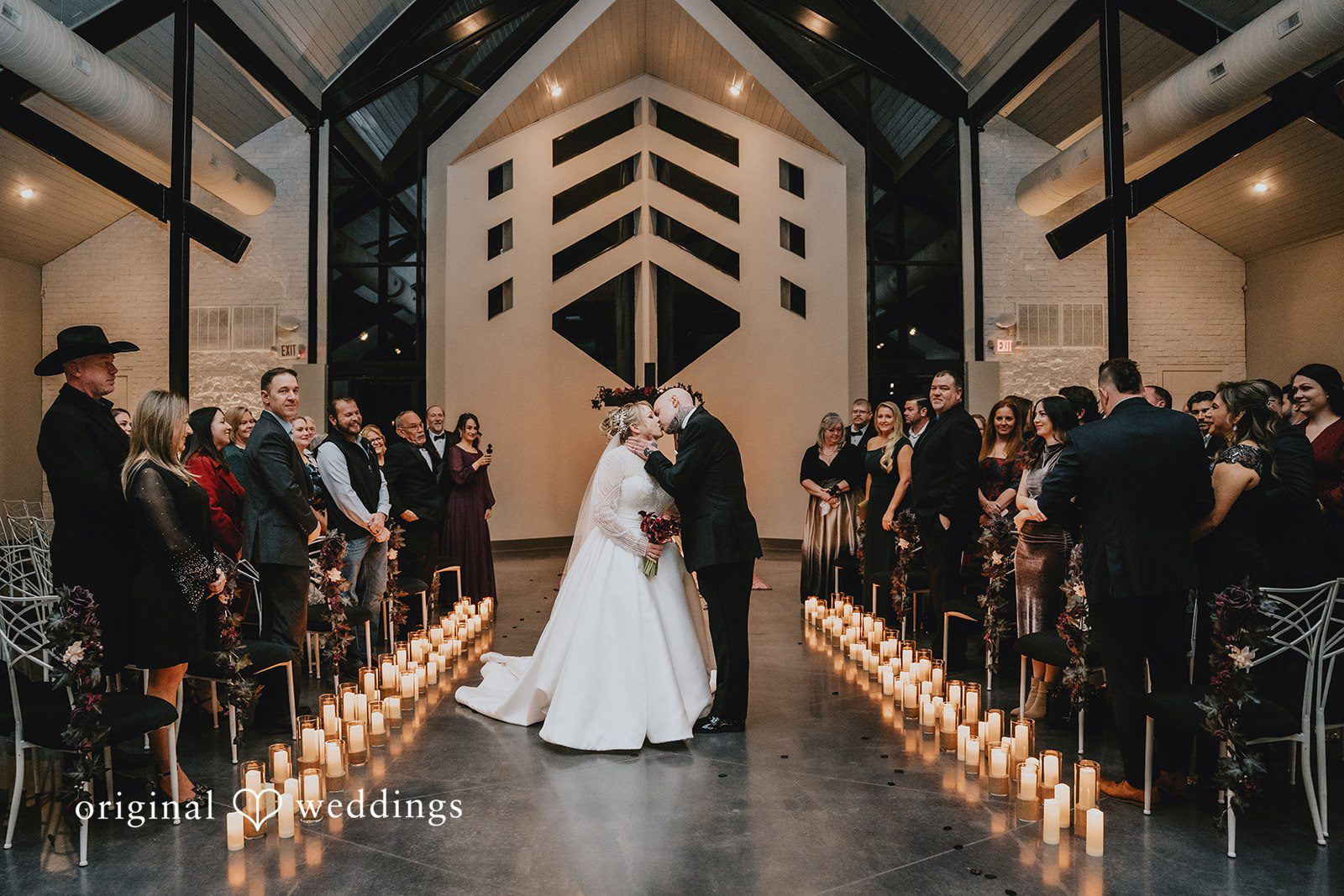 Married couple kissing in a candlelit chapel aisle.