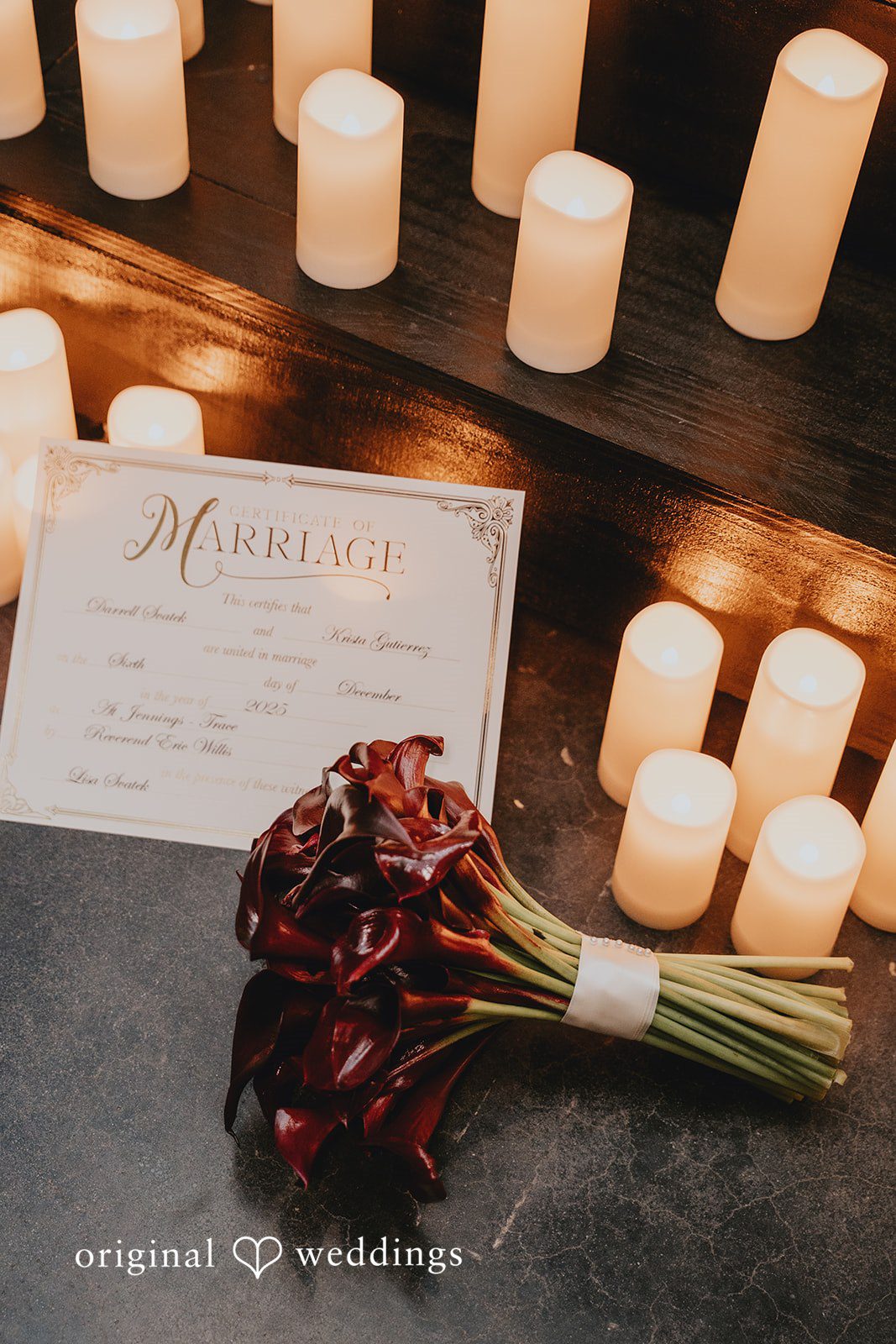 Dark red calla lily bouquet beside glowing candles.