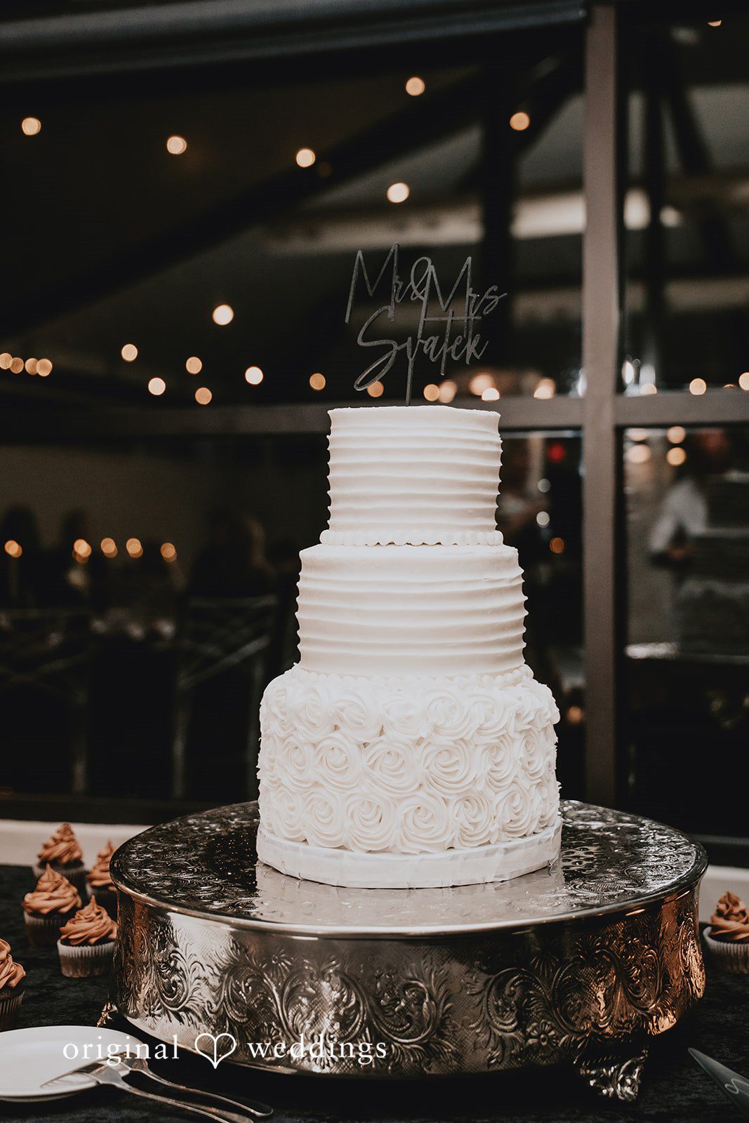 Three-tiered white wedding cake on silver stand.