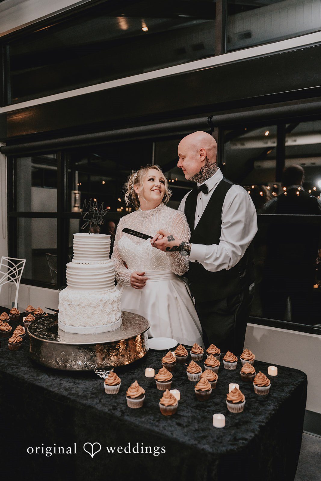 Newlyweds standing by wedding cake and dessert table.