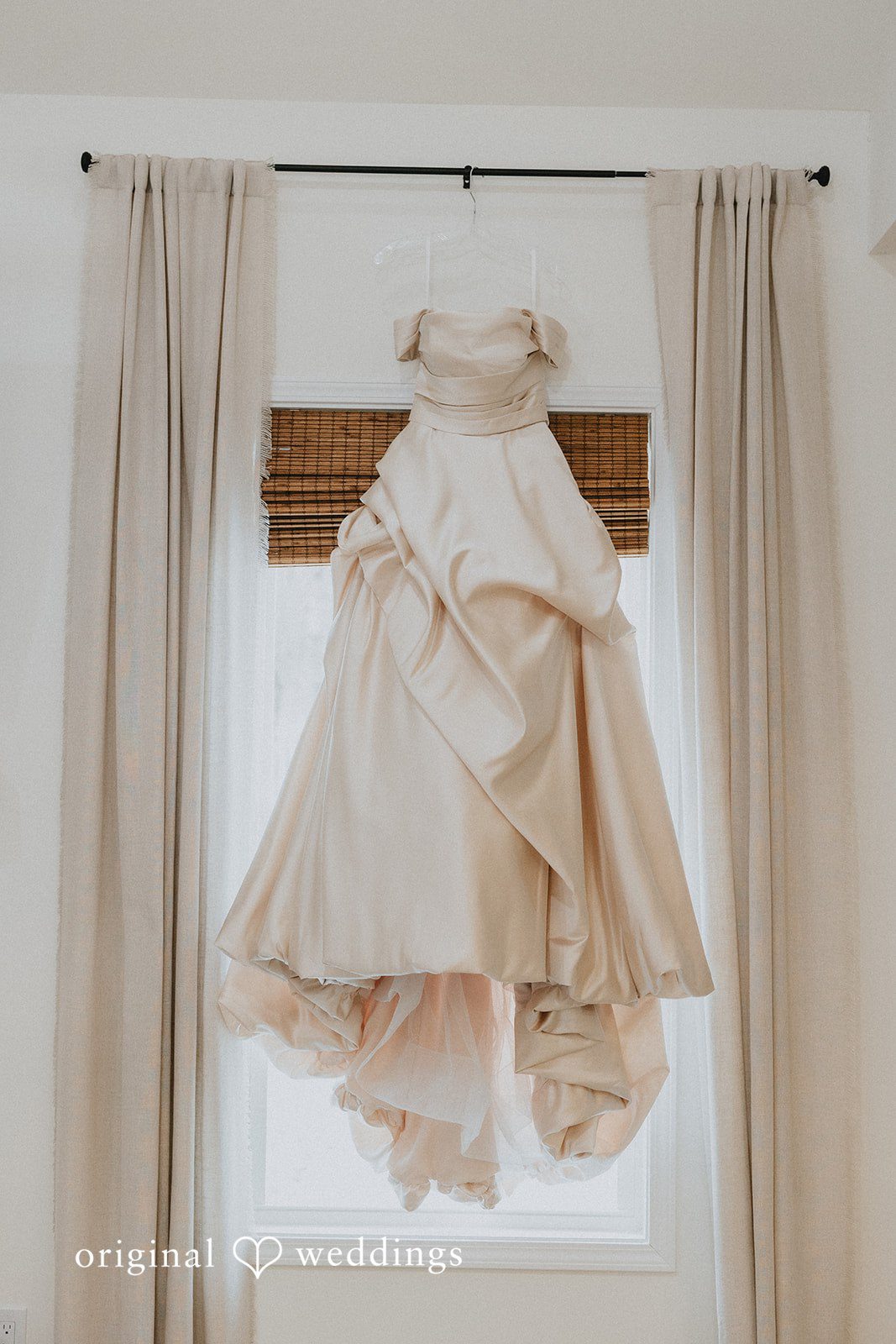 Ayana + Gabriel A white wedding gown hanging elegantly in front of a bright window.