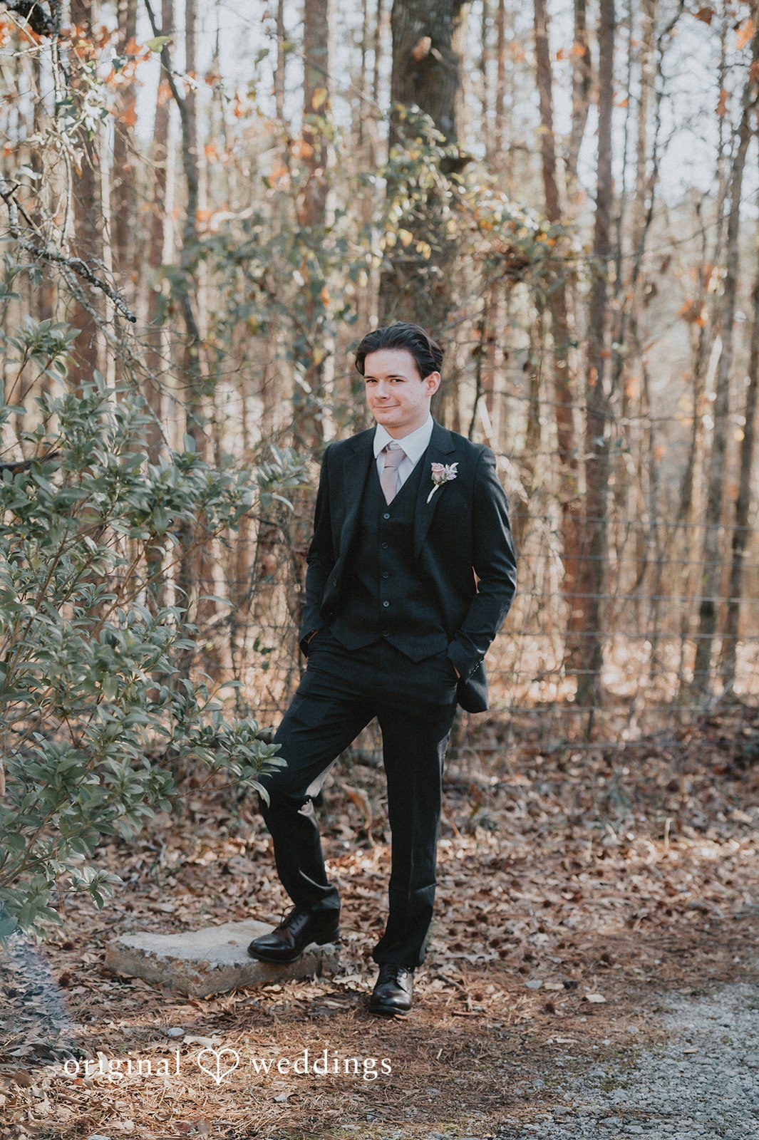 Ayana + Gabriel A groom posing in a black suit along a wooded trail at Lela's Place.