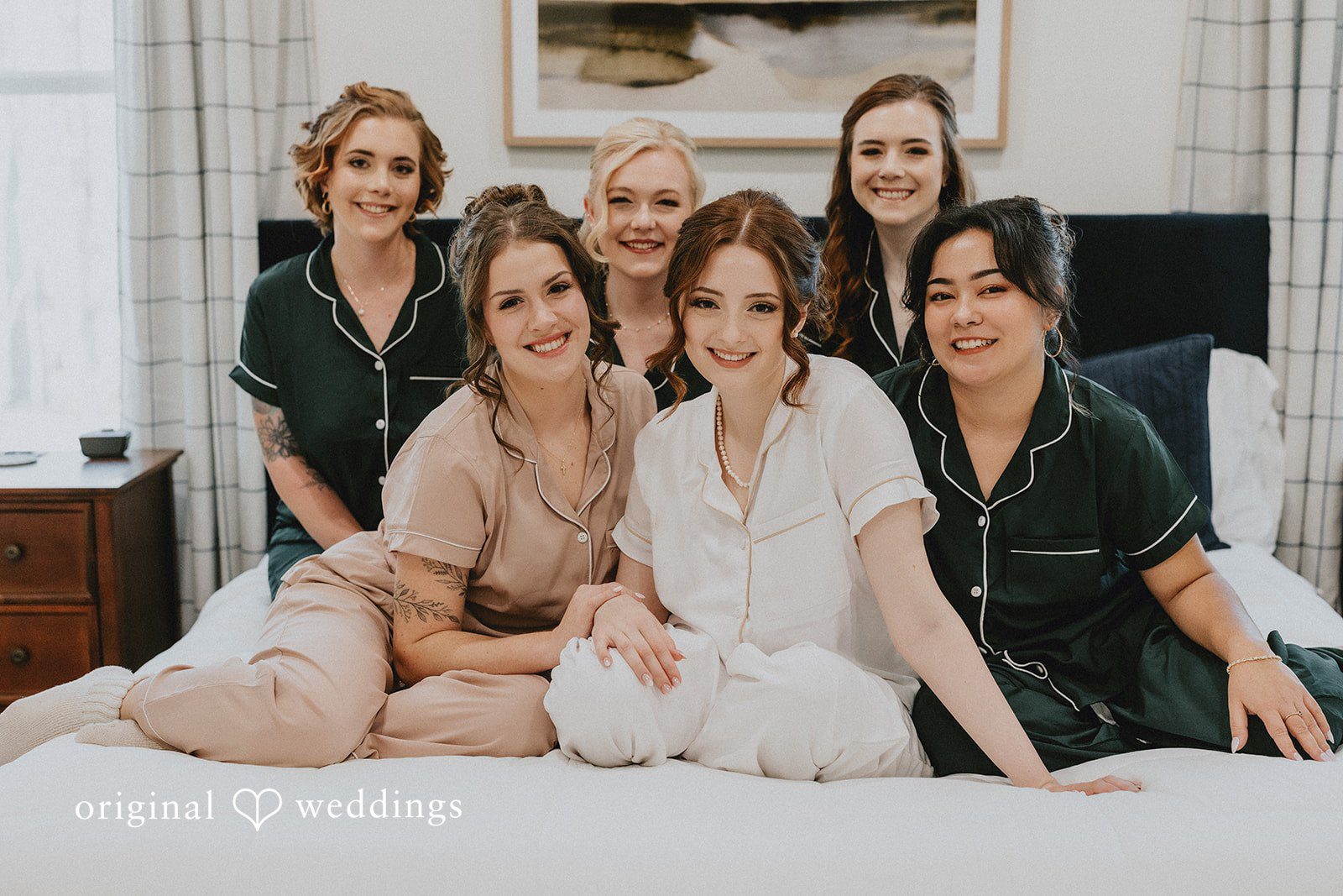 Ayana + Gabriel A bride smiling on a bed surrounded by her bridesmaids in matching pajamas.