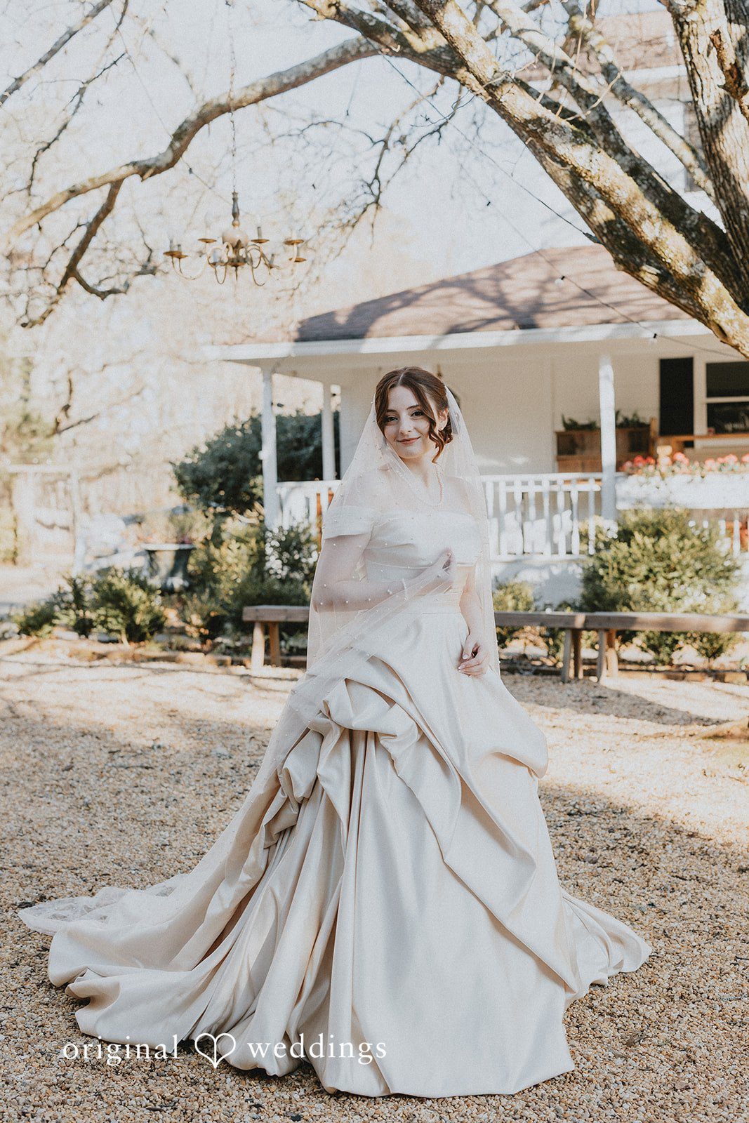 Ayana + Gabriel A bride standing on a path in her wedding gown with a house behind her.