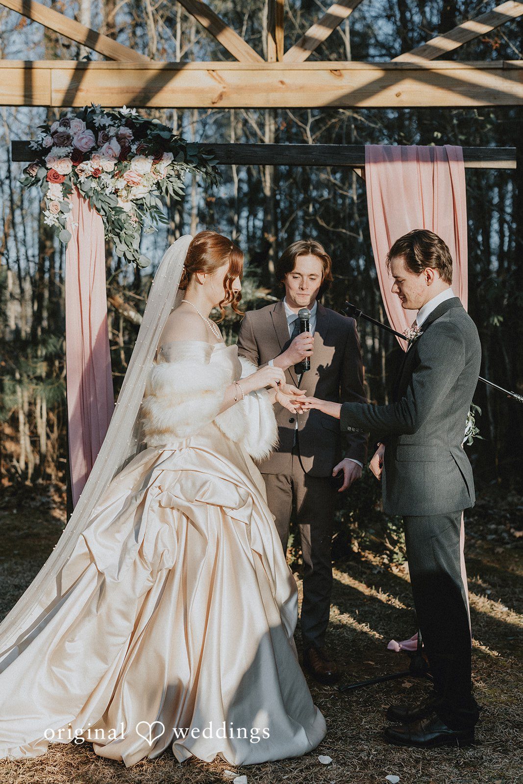 Ayana + Gabriel Couple exchanging rings under a wooden arbor during their ceremony.