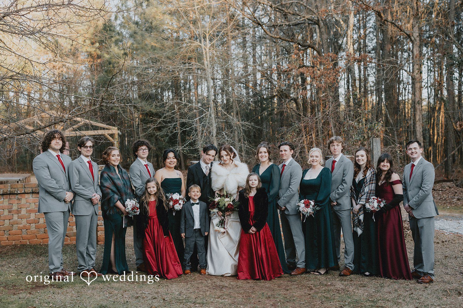 Ayana + Gabriel Large wedding party posing together for a group photo in front of trees.