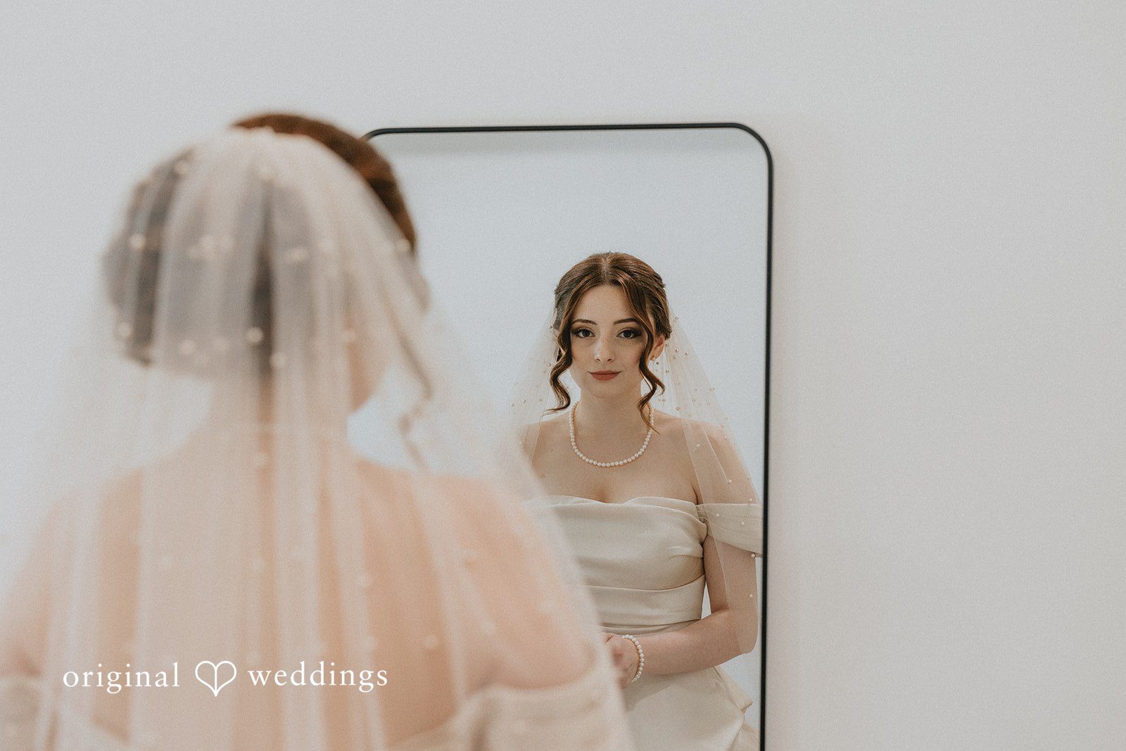 Ayana + Gabriel A bride wearing her veil and looking at her reflection in a mirror.