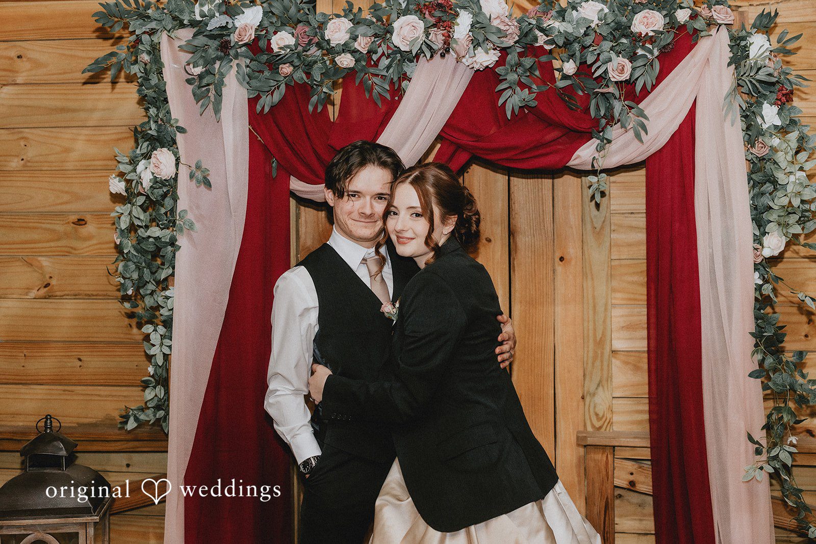 Ayana + Gabriel Bride and groom hugging closely in front of a draped wooden backdrop.