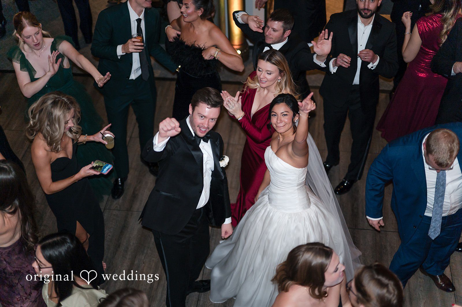 A bride and groom dancing on a crowded dance floor surrounded by wedding guests.