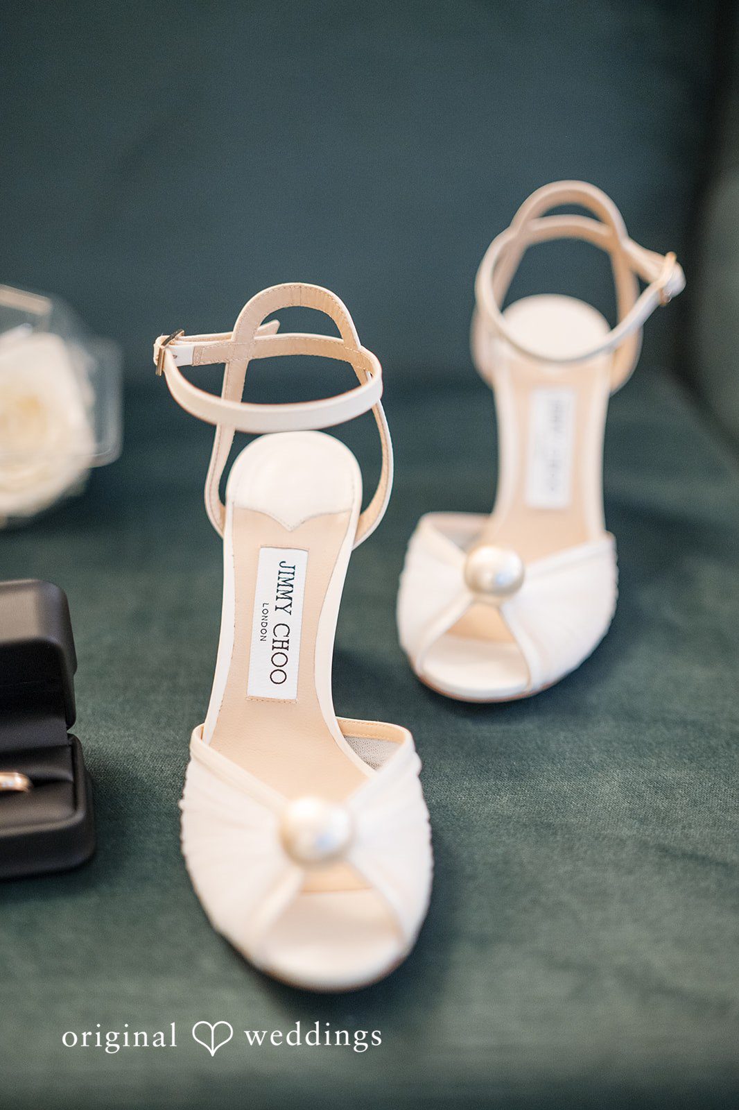 A pair of white high-heeled bridal shoes with ankle straps and pearl details.