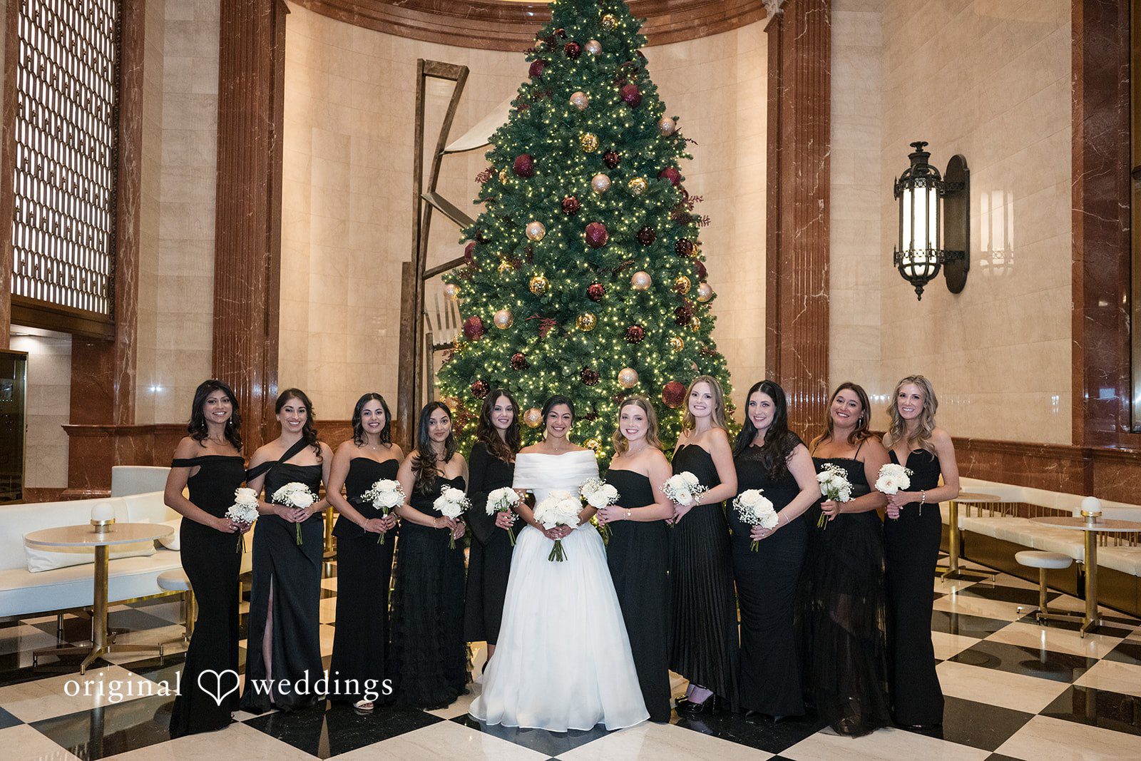 A bridal party standing together in front of a tall, decorated holiday tree at Library at 190.