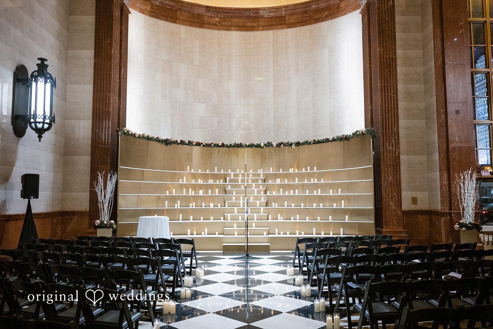 A wedding ceremony setup with rows of black chairs facing a large draped altar.