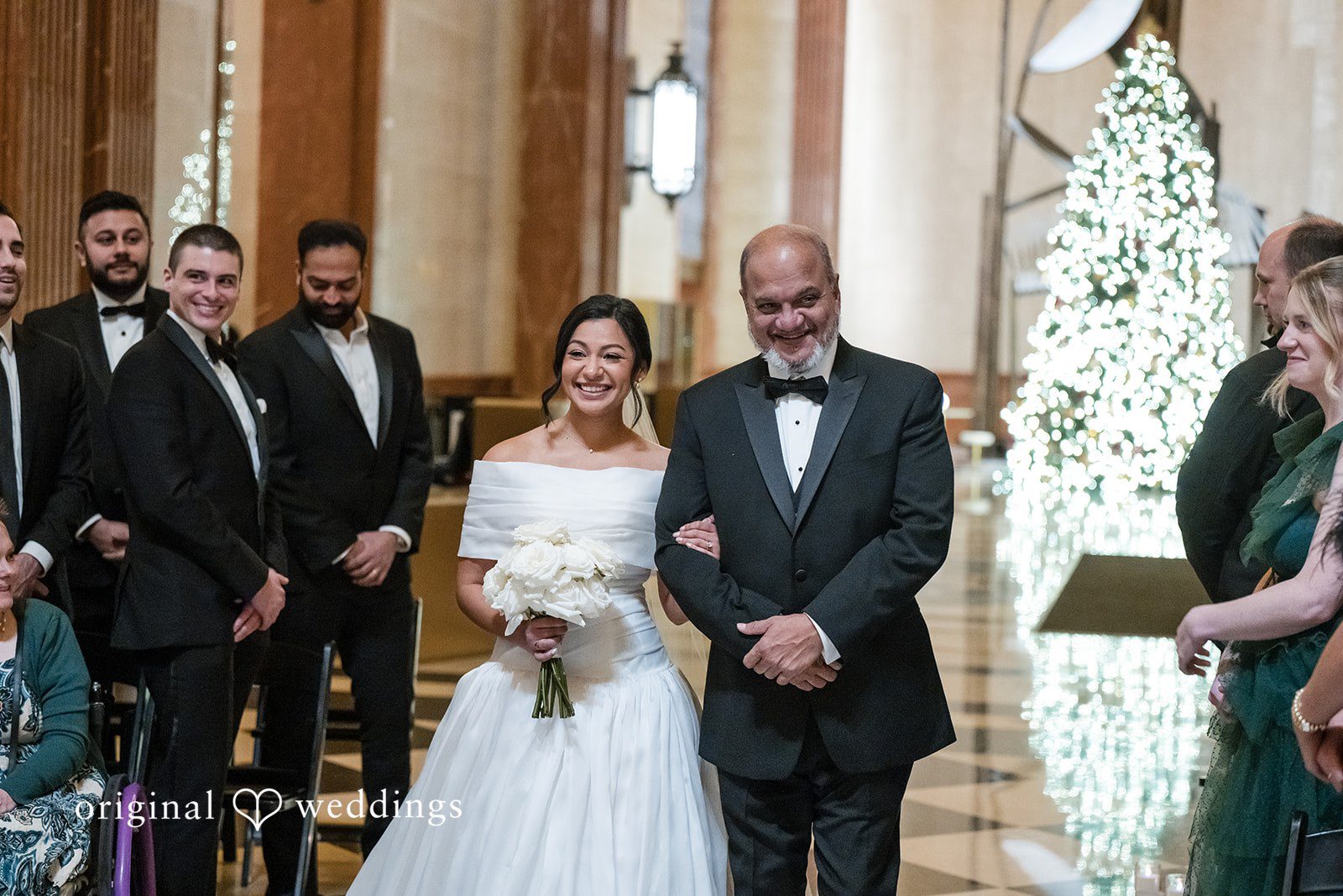 A bride walking down the aisle in a white gown accompanied by a man in a tuxedo.