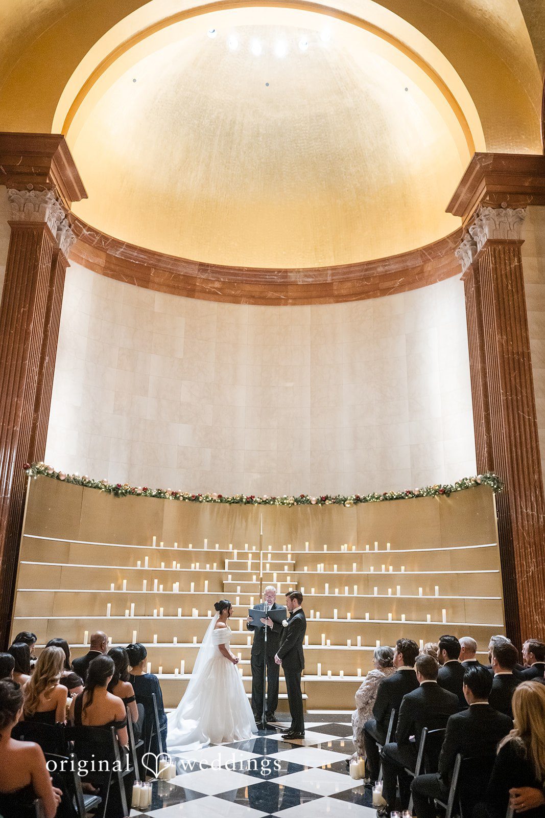 A wide shot of a wedding ceremony in a large hall with guests seated in rows.