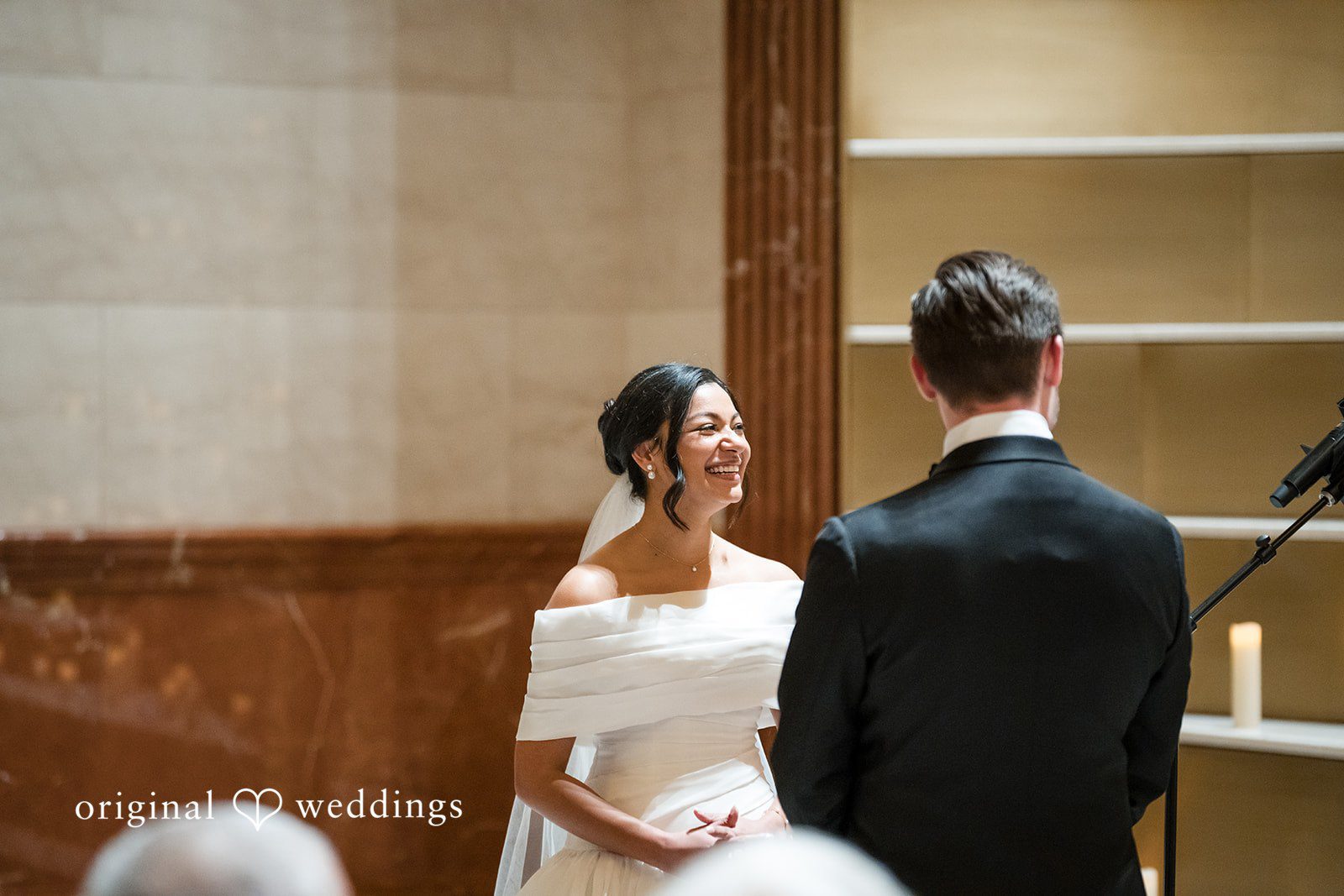 bride in an off-the-shoulder gown smiling up at the groom during their wedding ceremony.