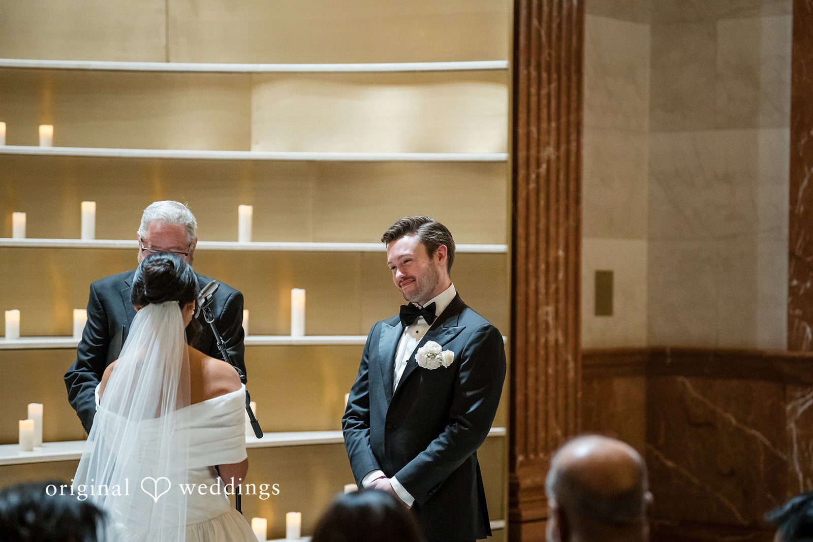 A groom smiling at the altar while the bride walks toward him.