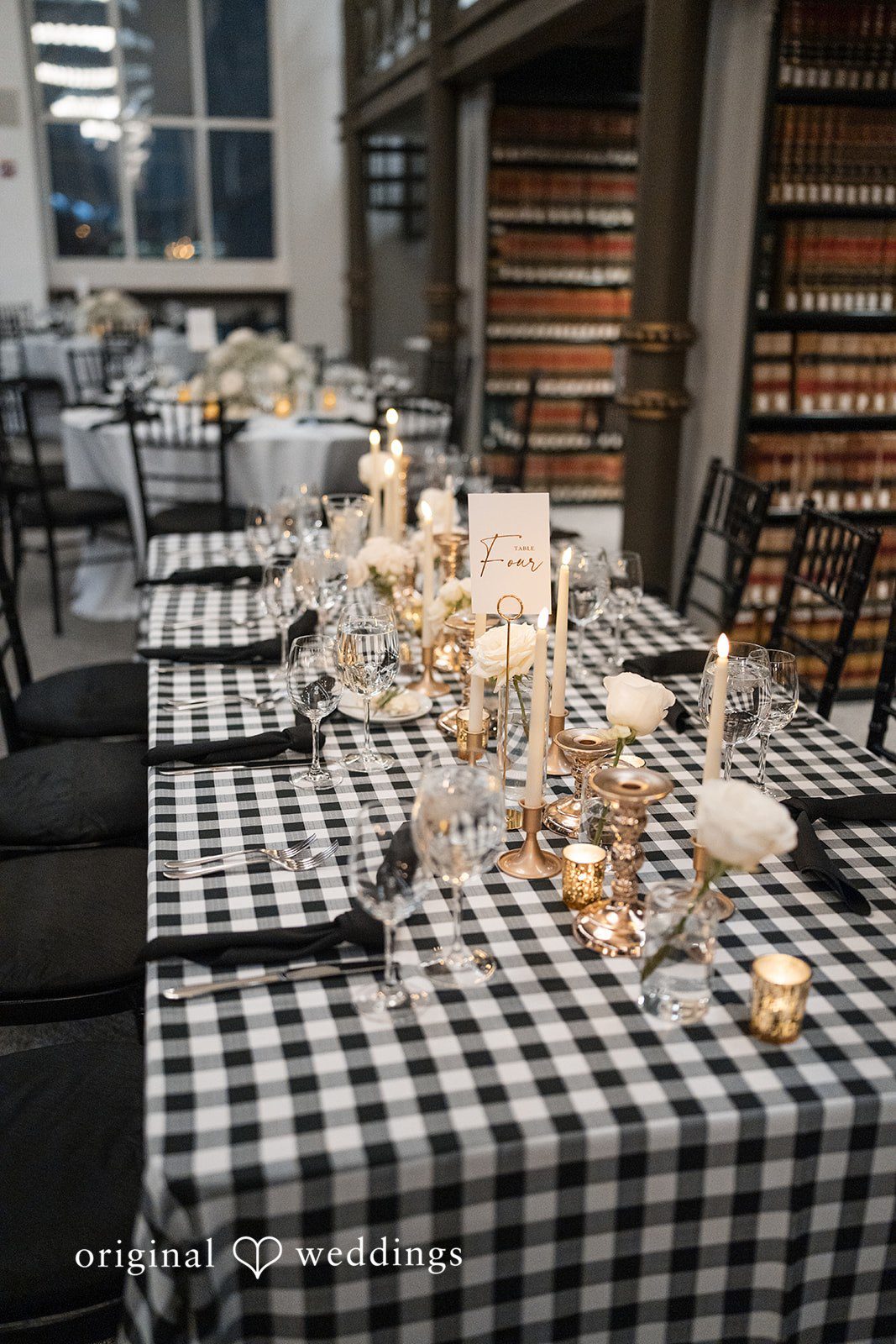 A long dining table set with a black and white checkered tablecloth and glowing candles.