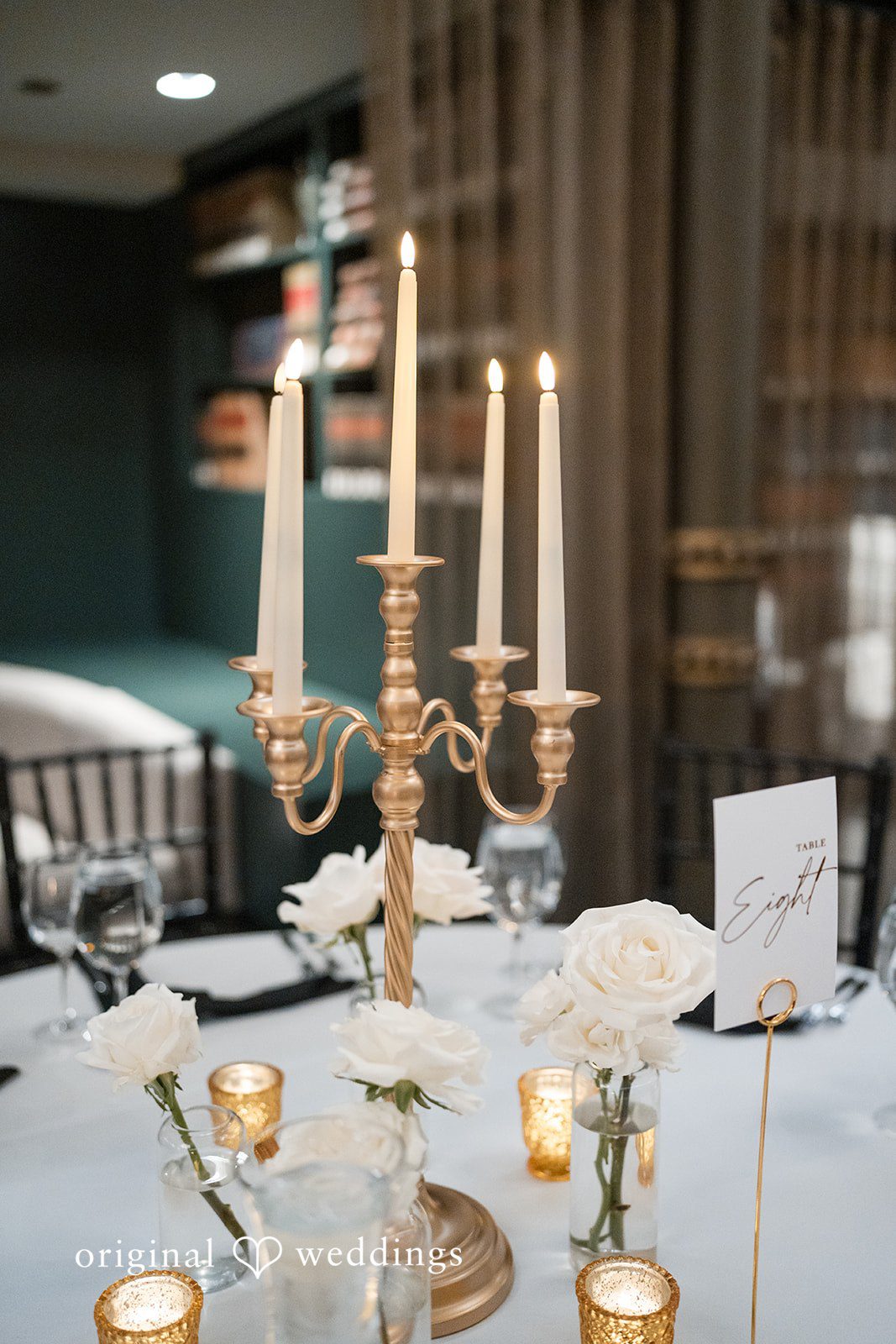 A decorated reception table featuring a gold candelabra with lit candles and floral arrangements at Library at 190.