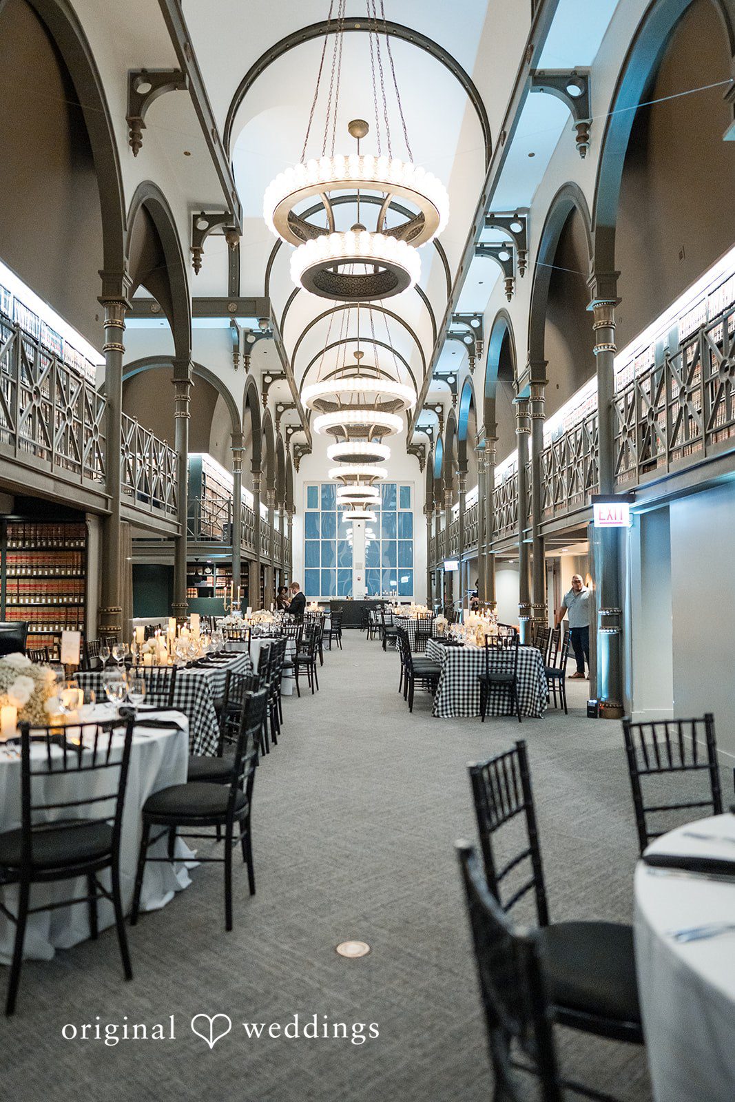 A long reception hall with arched ceilings, dining tables, and black chairs.