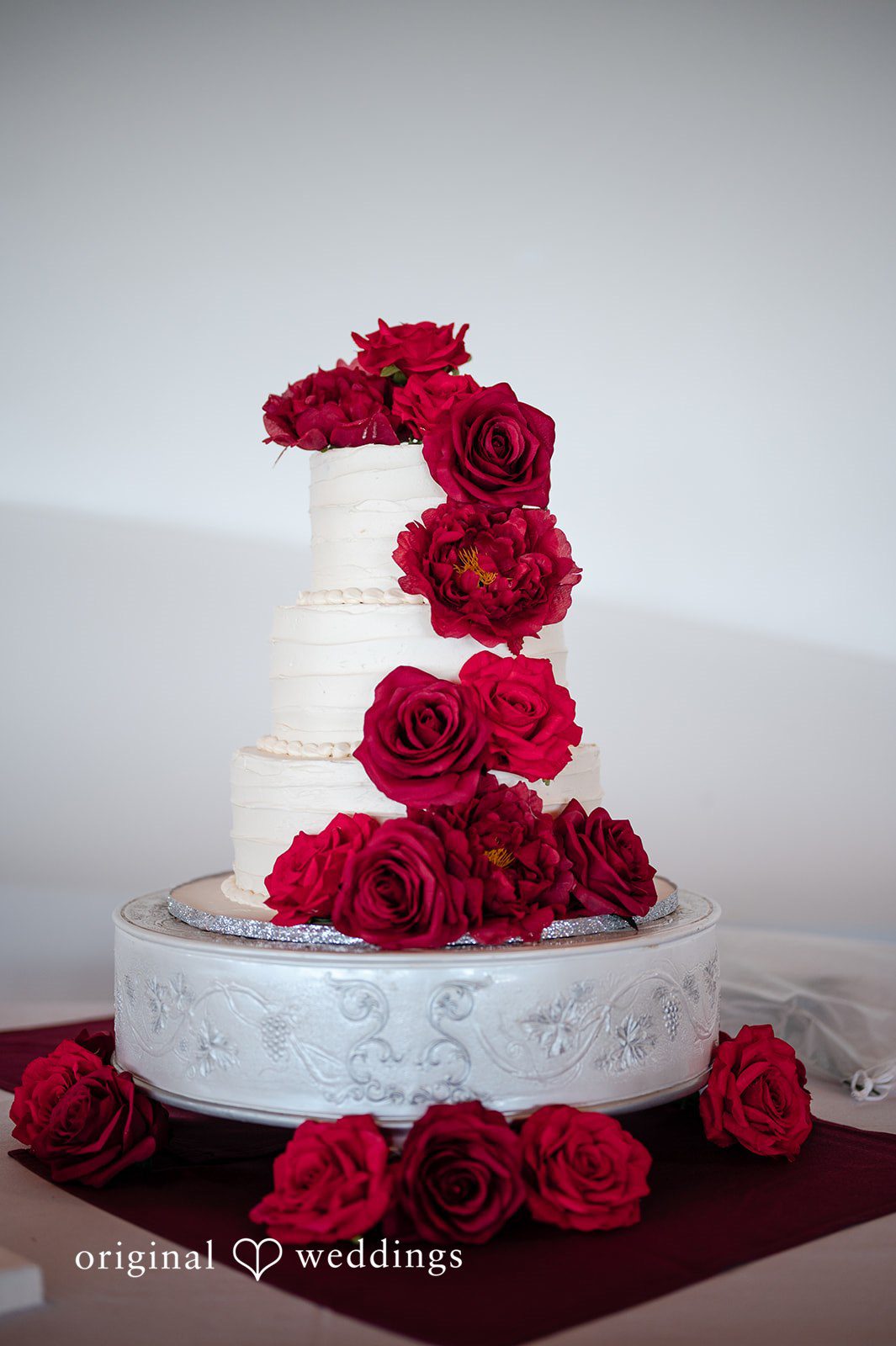 An all-white wedding cake adorned with red blooms
