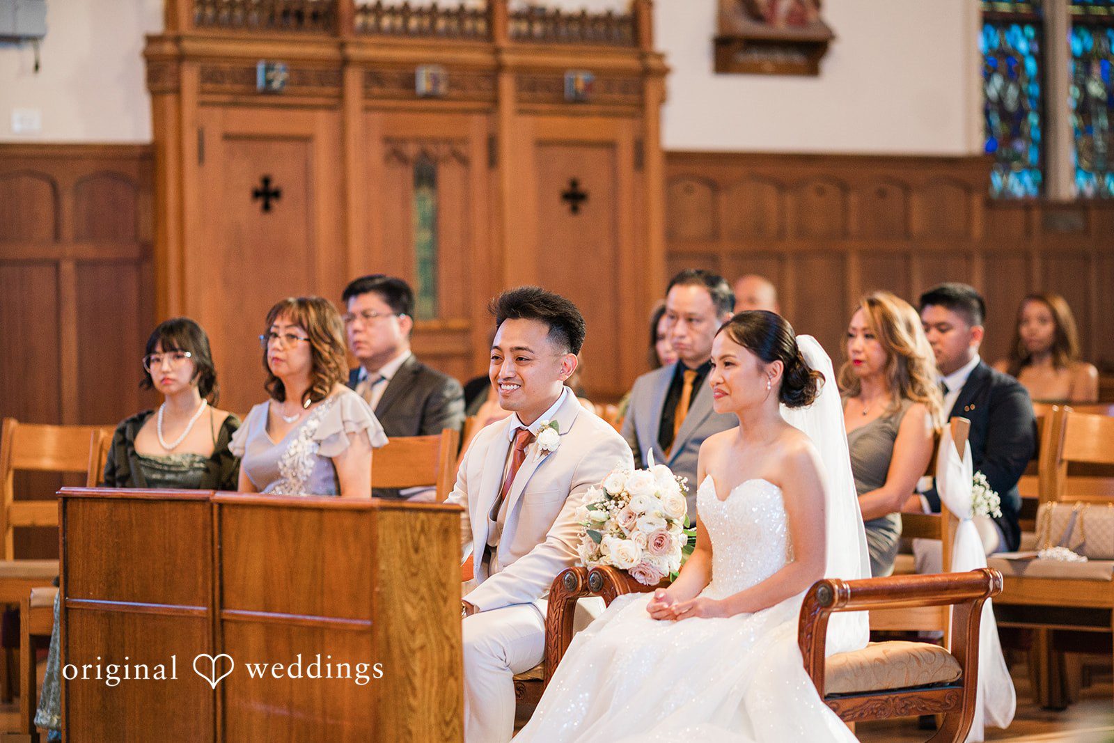 Charize Giann + Mark Shou Bride and groom sitting together during a heartfelt church wedding ceremony surrounded by family and guests at Palm Event Center captured by San Francisco wedding photographers from Original Weddings