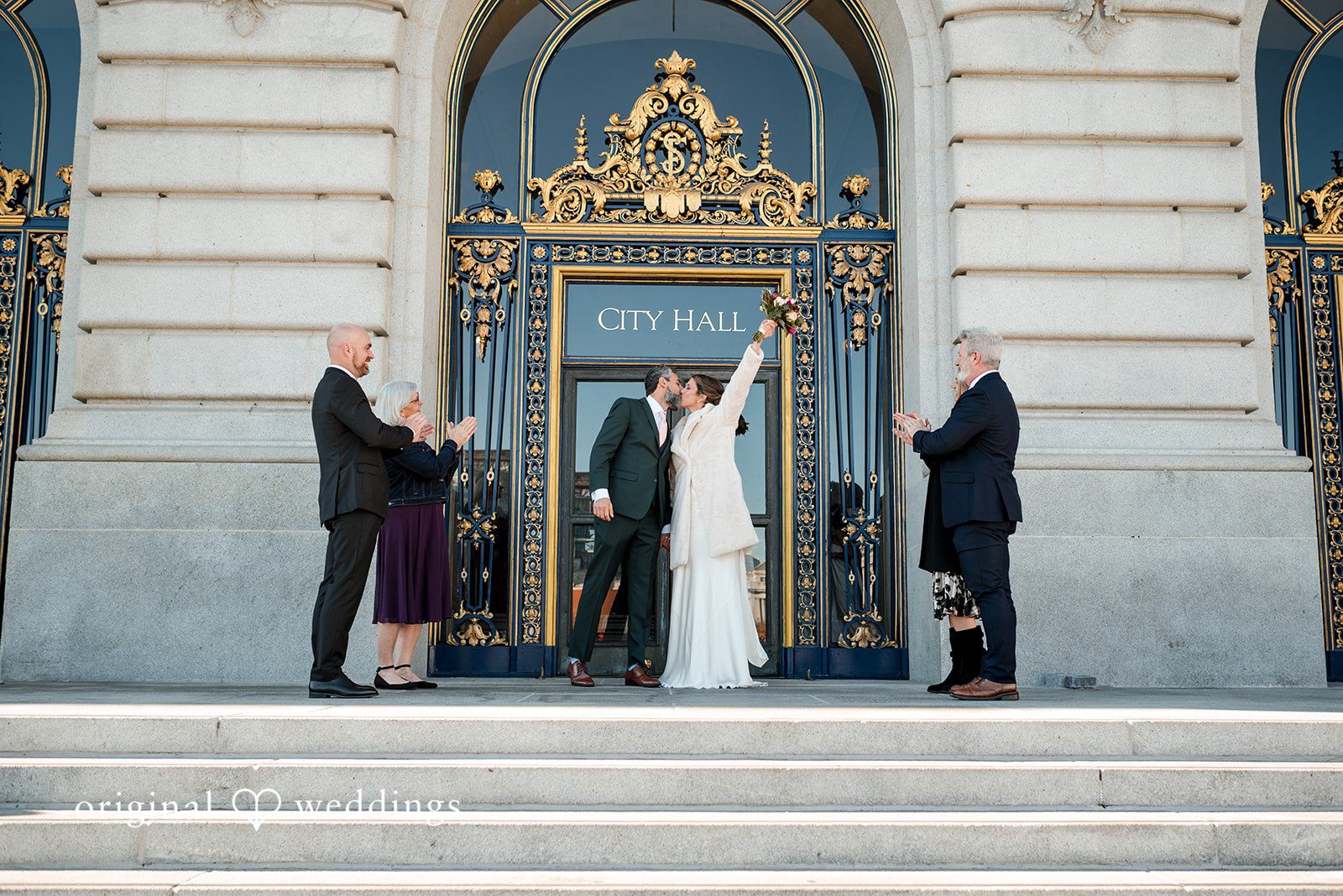 The couple shares a romantic kiss in front of the City Hall with cheers from family