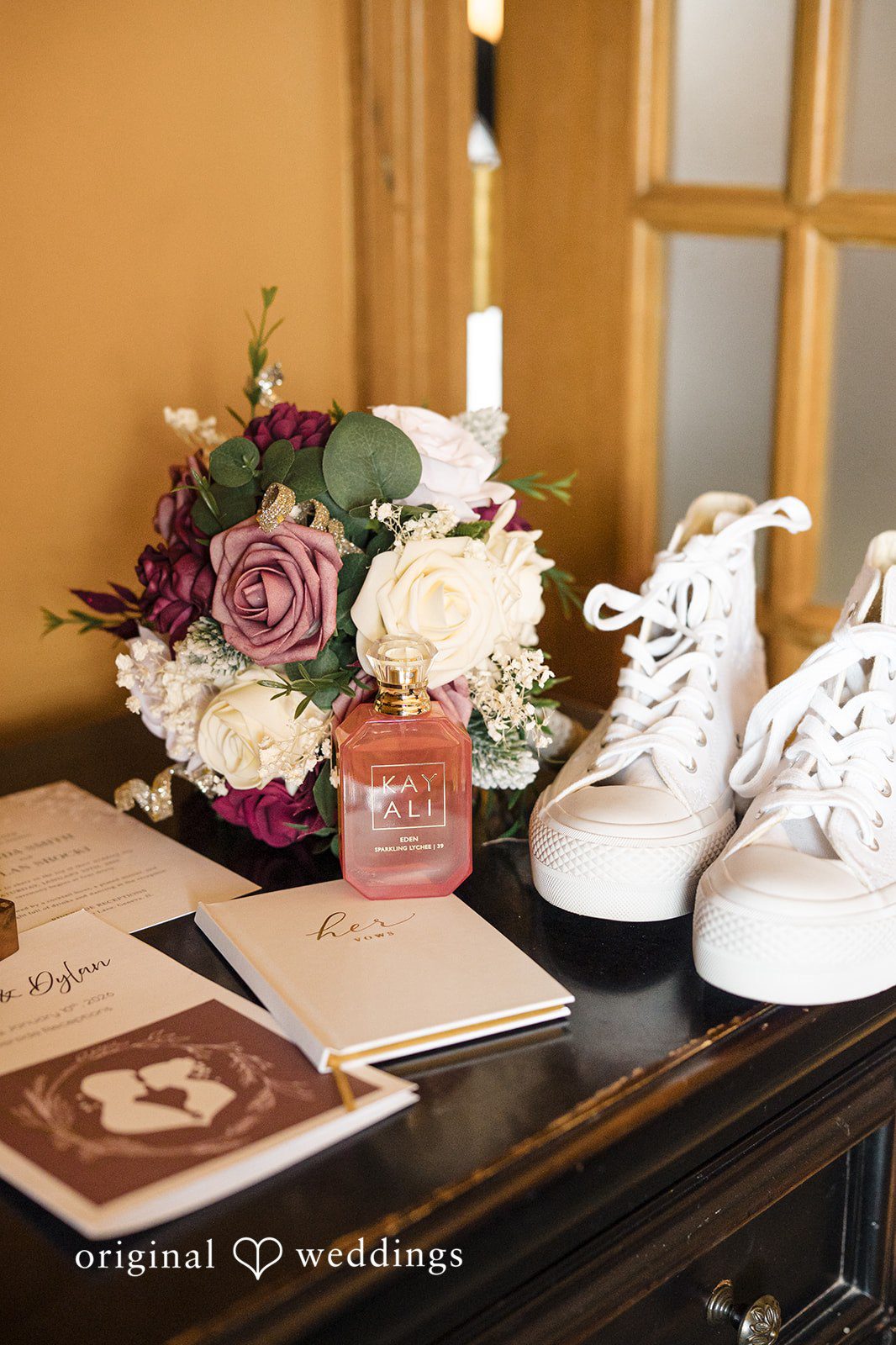 Wedding detail flat lay with shoes, perfume, bouquet, and invitation
