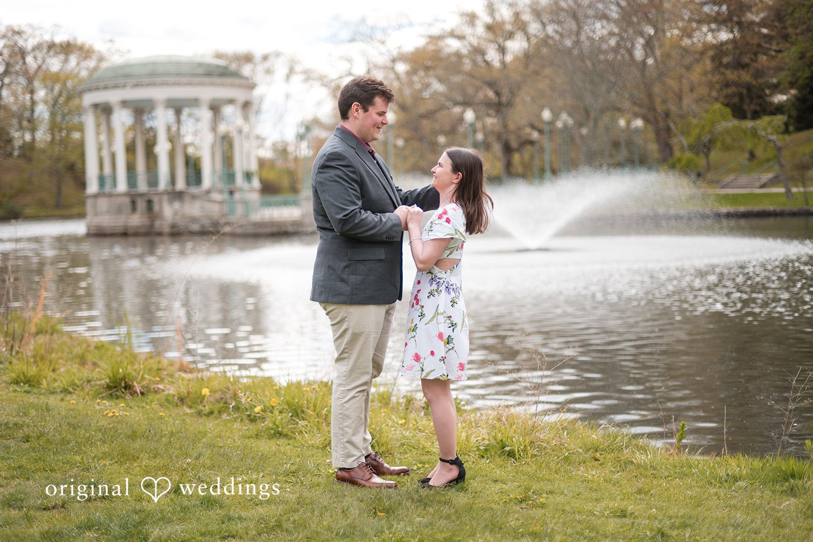 Engagement Photography Services capturing couple standing by water while holding hands and looking at each other  at Roger Williams Park by Original Weddings