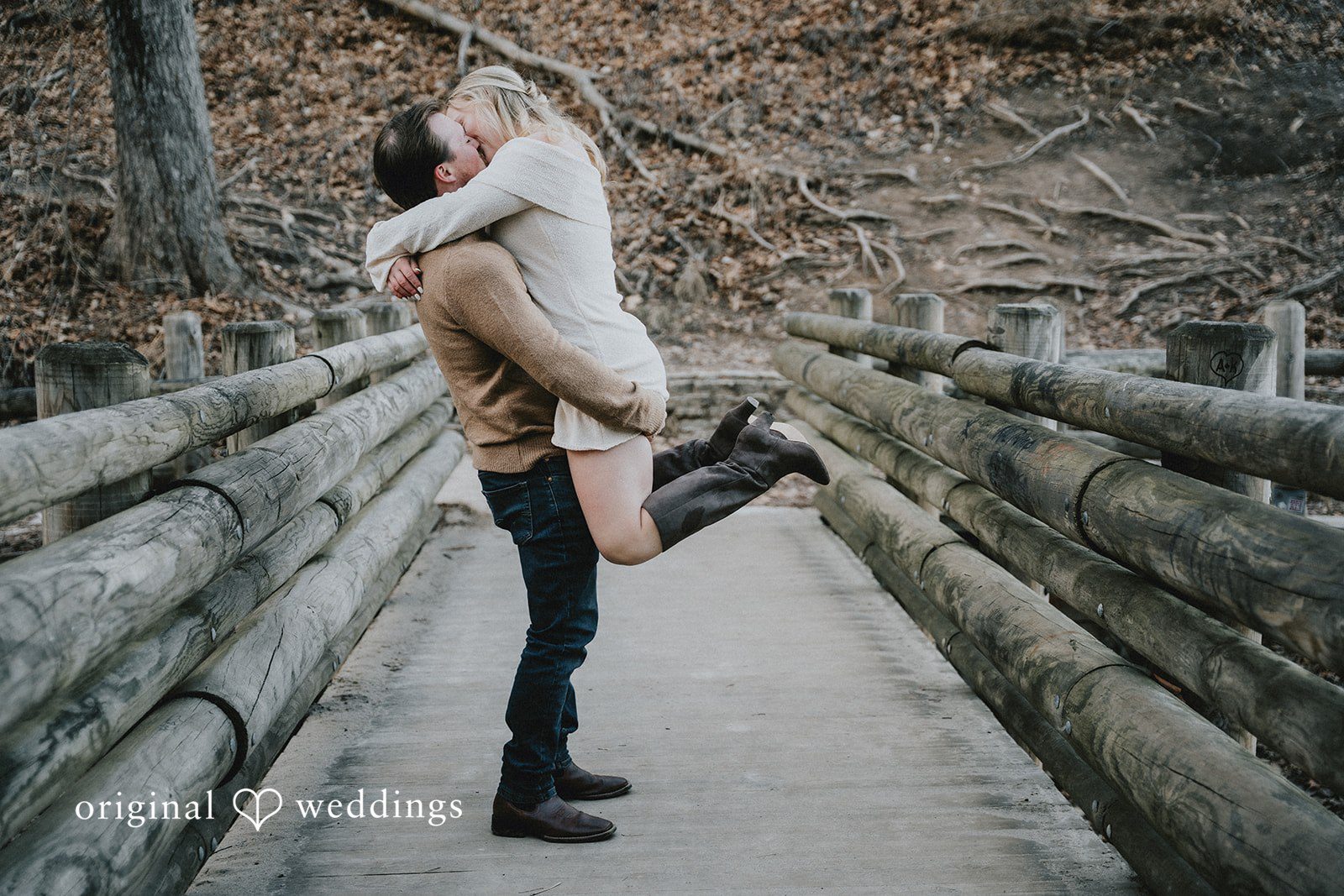The man lifting the woman into the air while standing on a wooden bridge