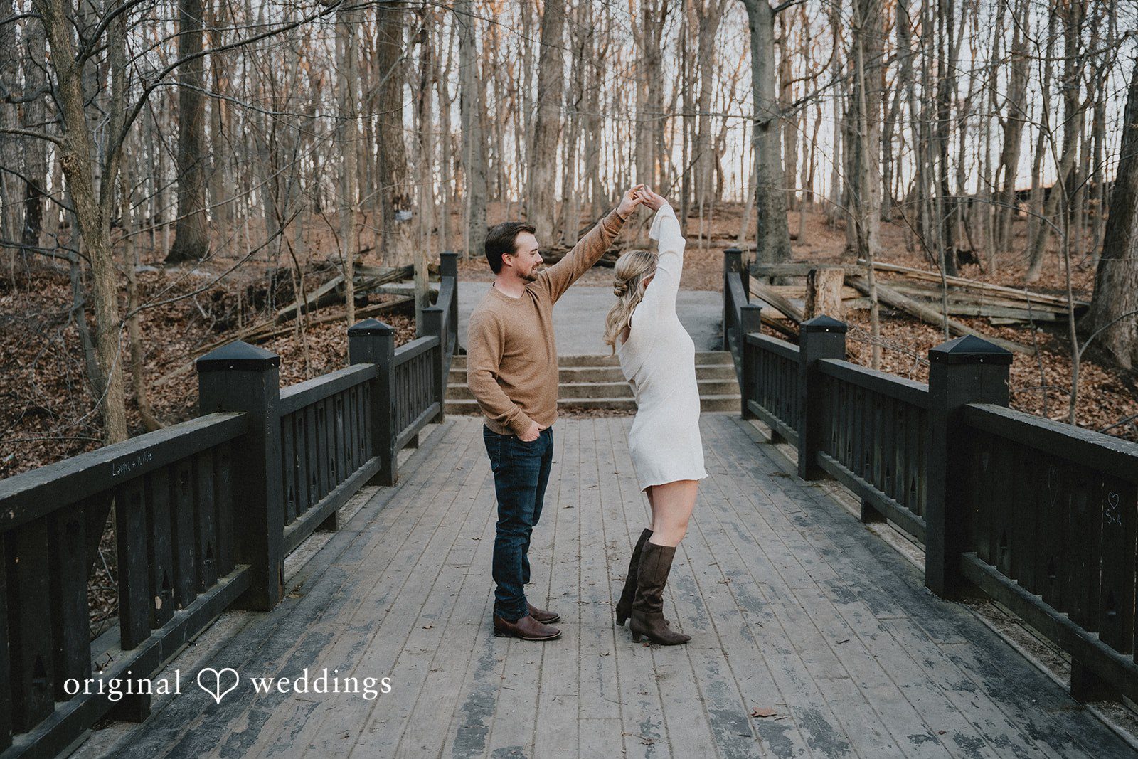 Couple holding hands and dancing on a dark wooden bridge.