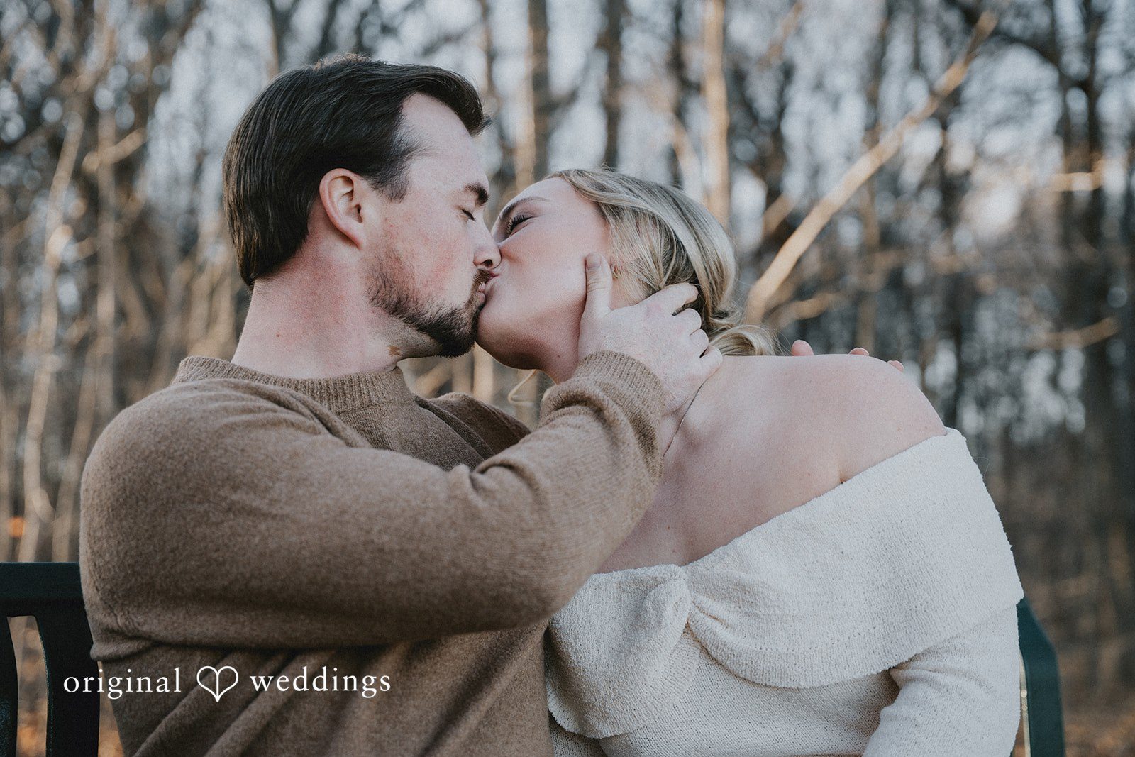 A romantic shot of the couple kissing in a soft-focus forest setting.